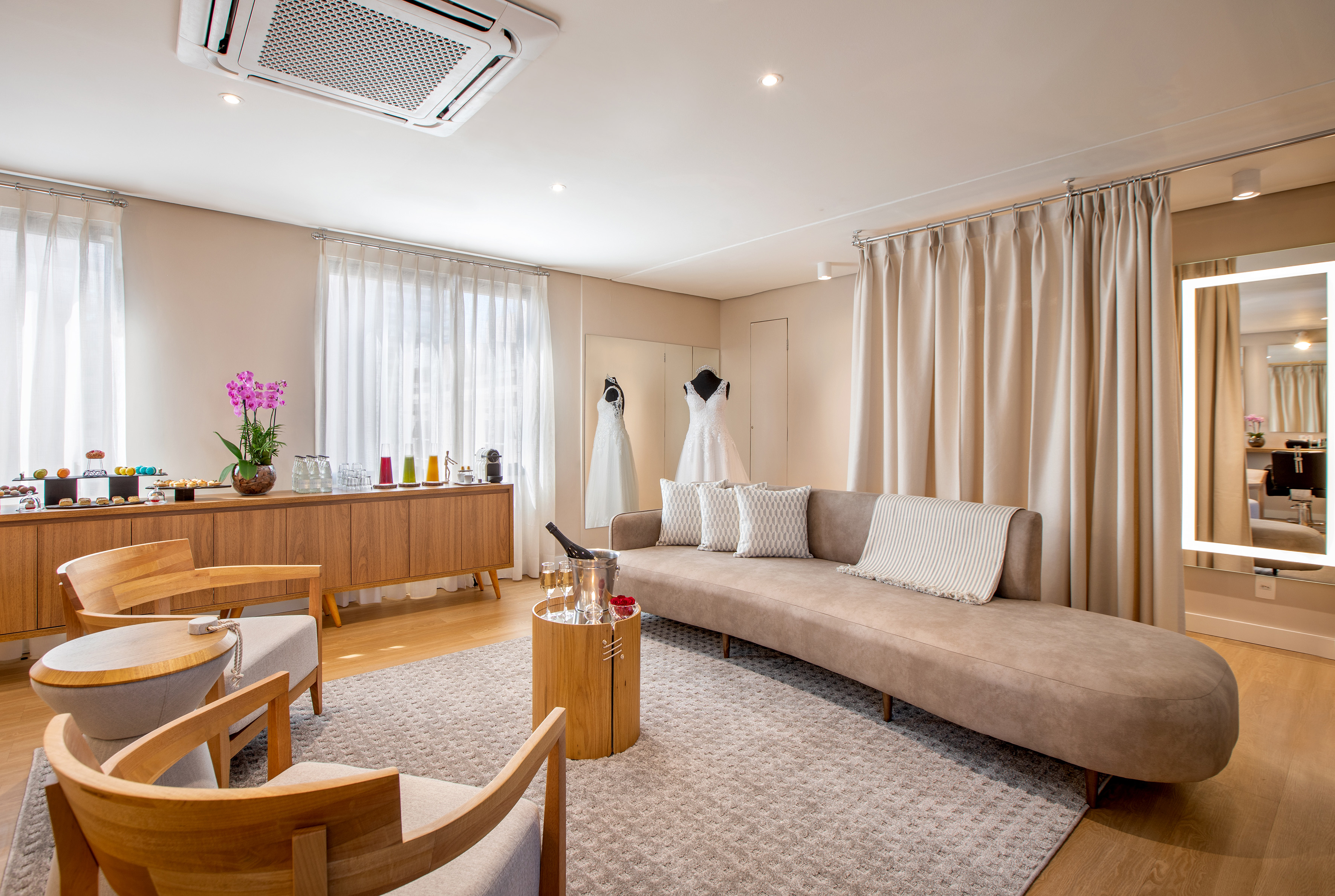 Elegant bridal suite with wedding dresses, modern sofa, and refreshment bar.