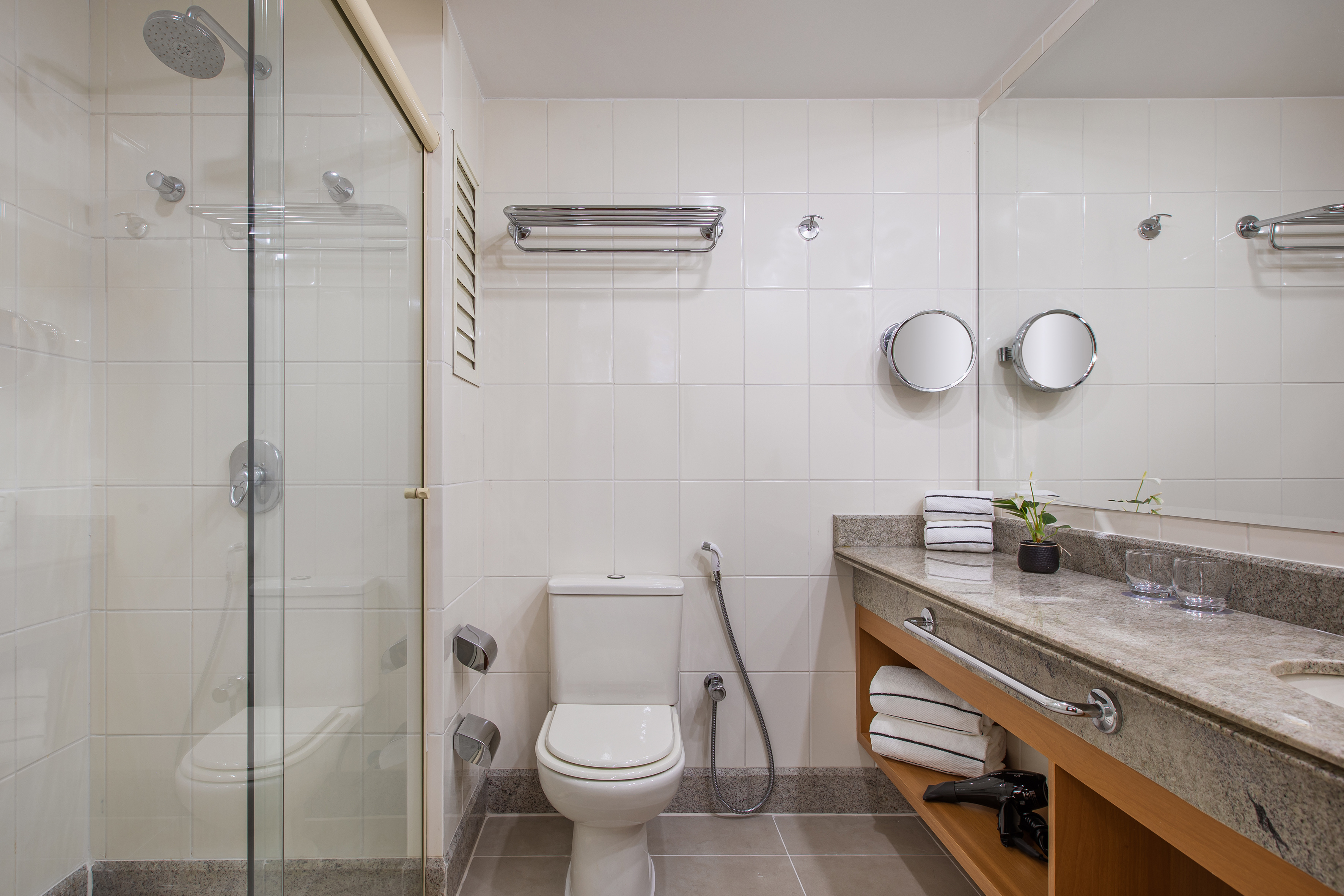 Hotel bathroom with glass shower, toilet, granite vanity, and clean towels.