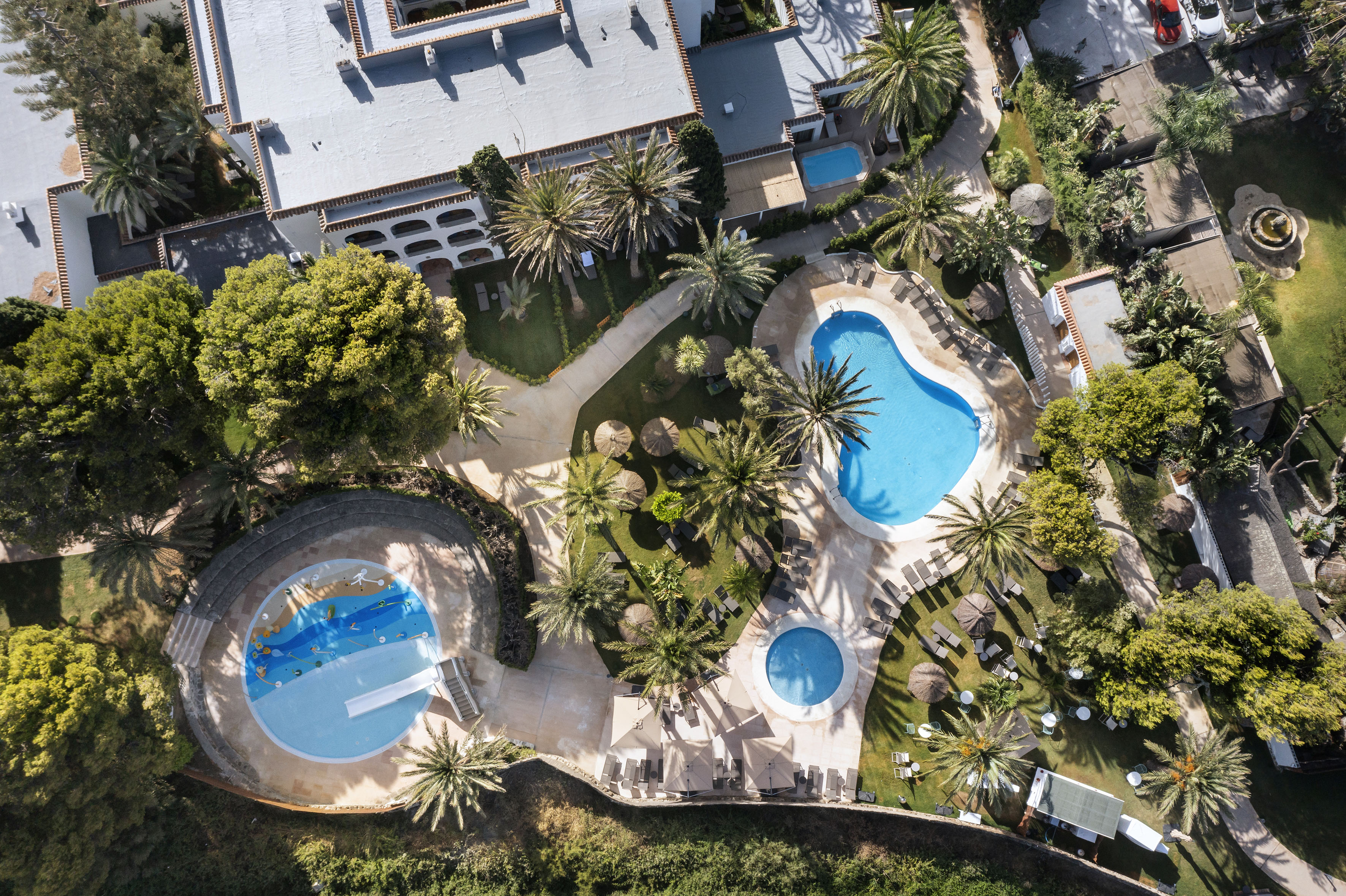 Aerial view of tropical hotel resort with multiple pools and palm trees.