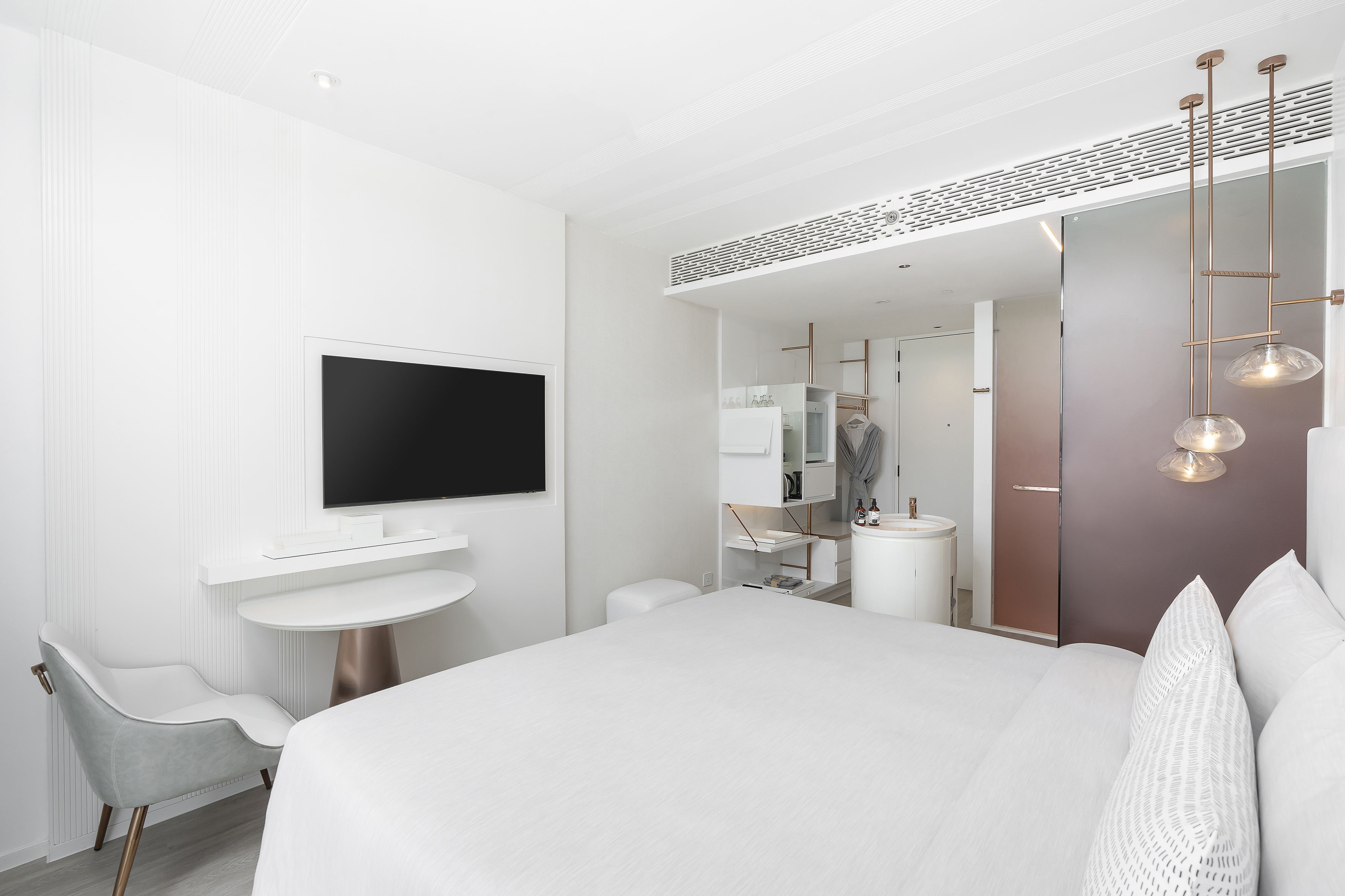 Minimalist hotel room with white bed, wall-mounted TV, and modern furnishings.