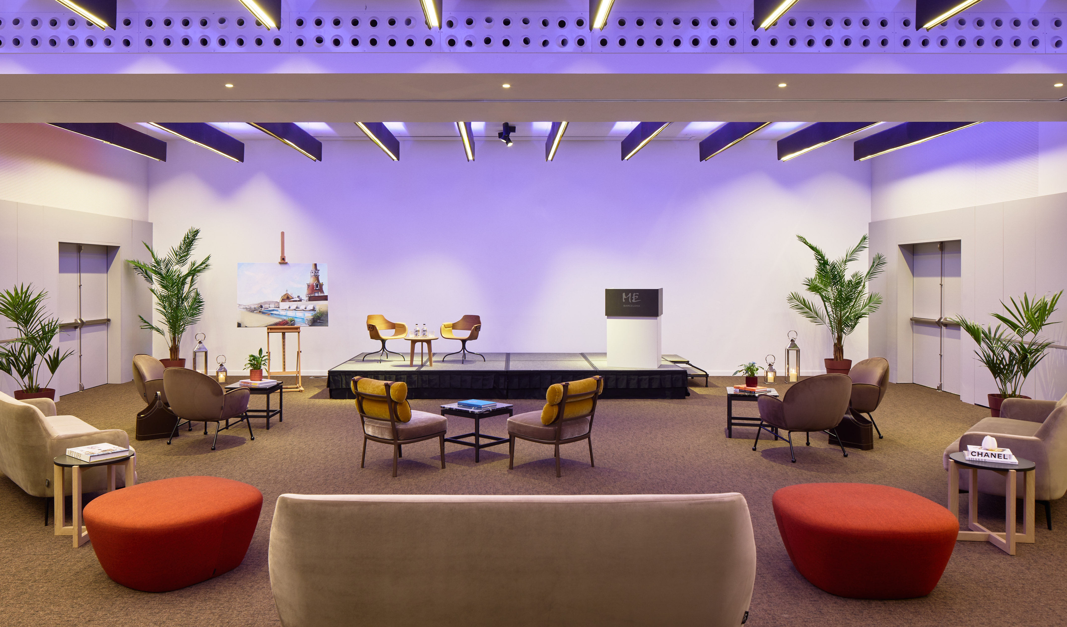 Modern event hall with stage, podium, diverse lounge seating, purple lighting.