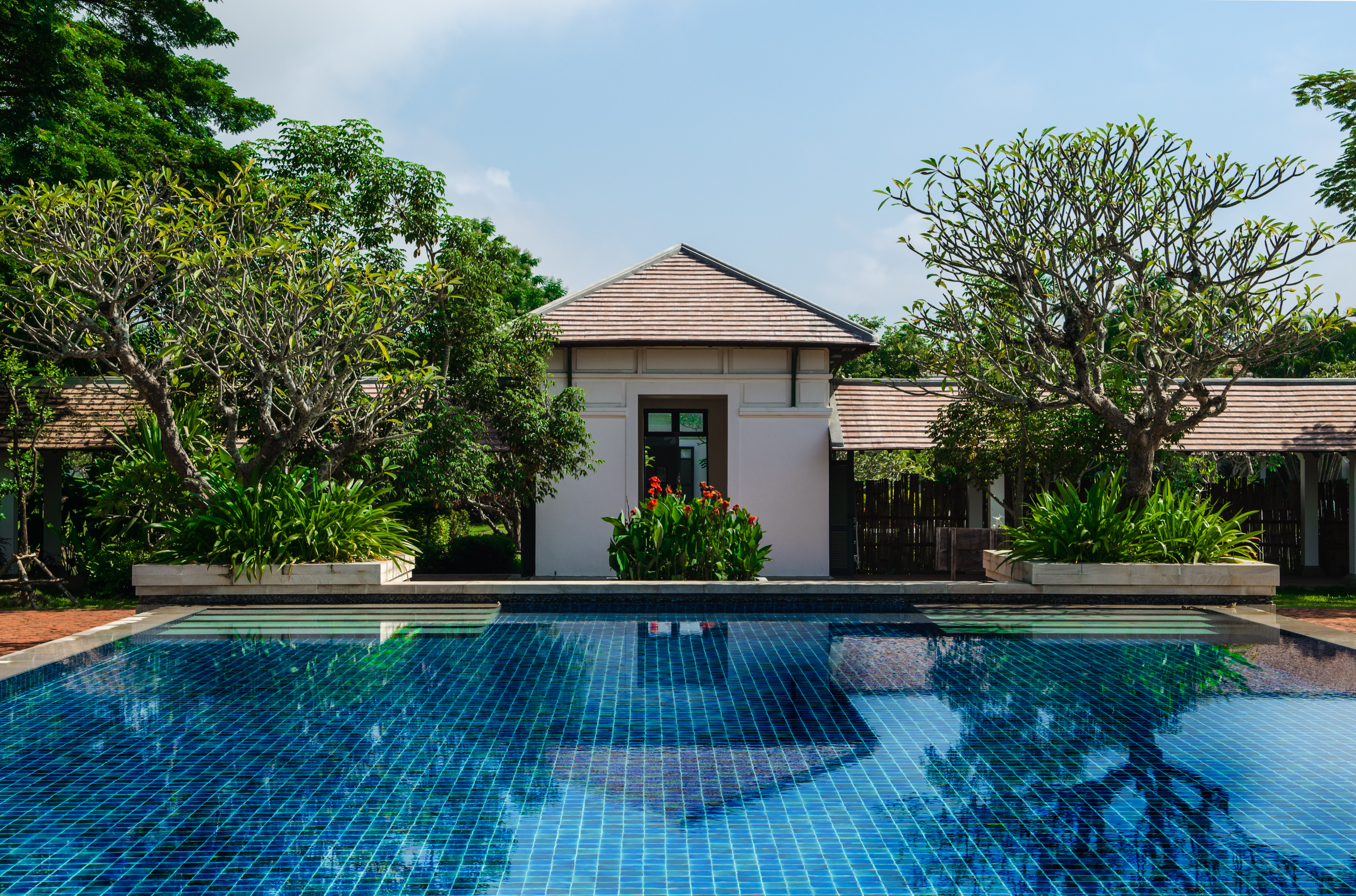 Luxury resort swimming pool with white villa, tropical garden, red flowers.