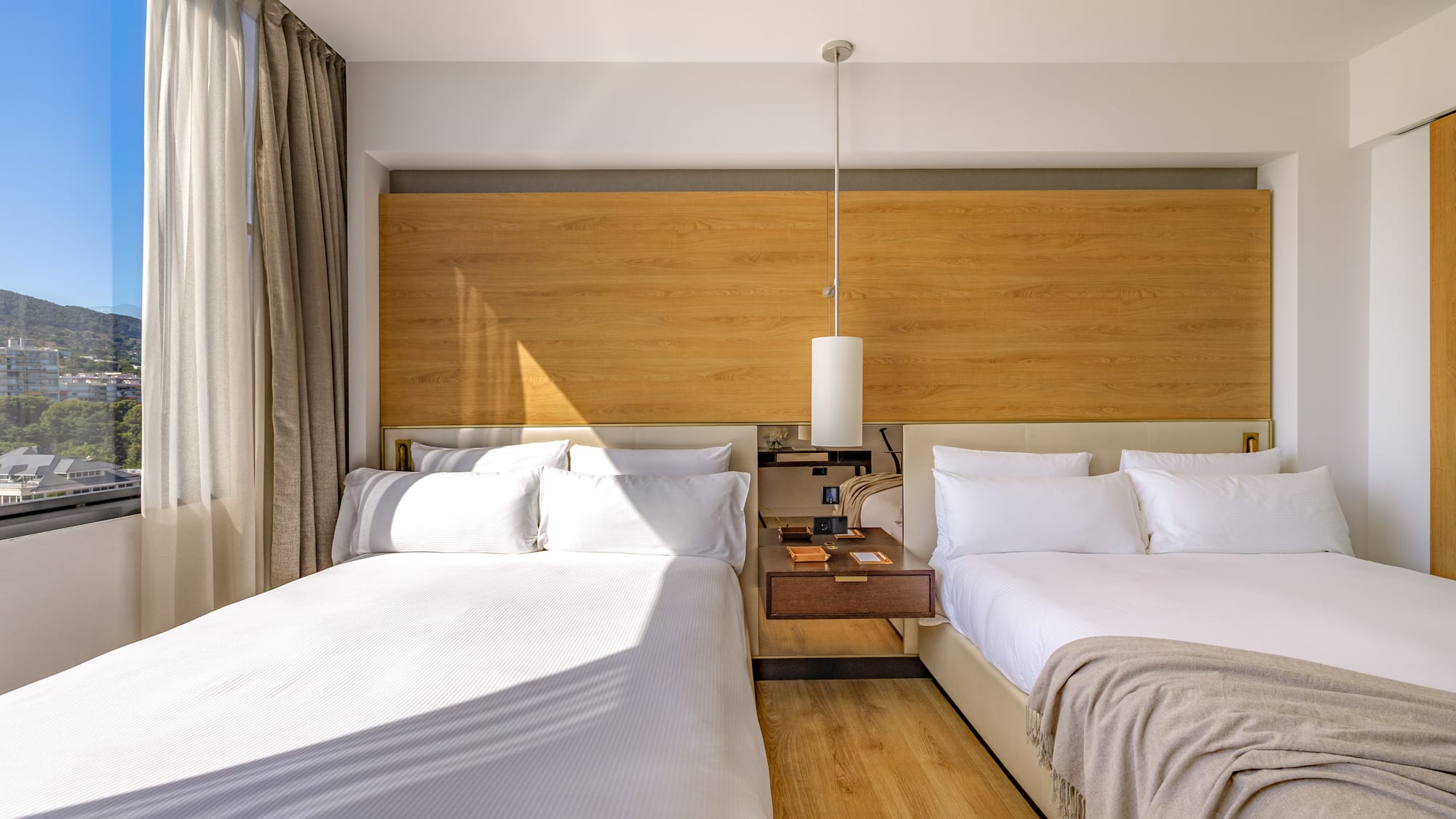 Modern hotel room with two beds, wooden headboard, and scenic mountain view.