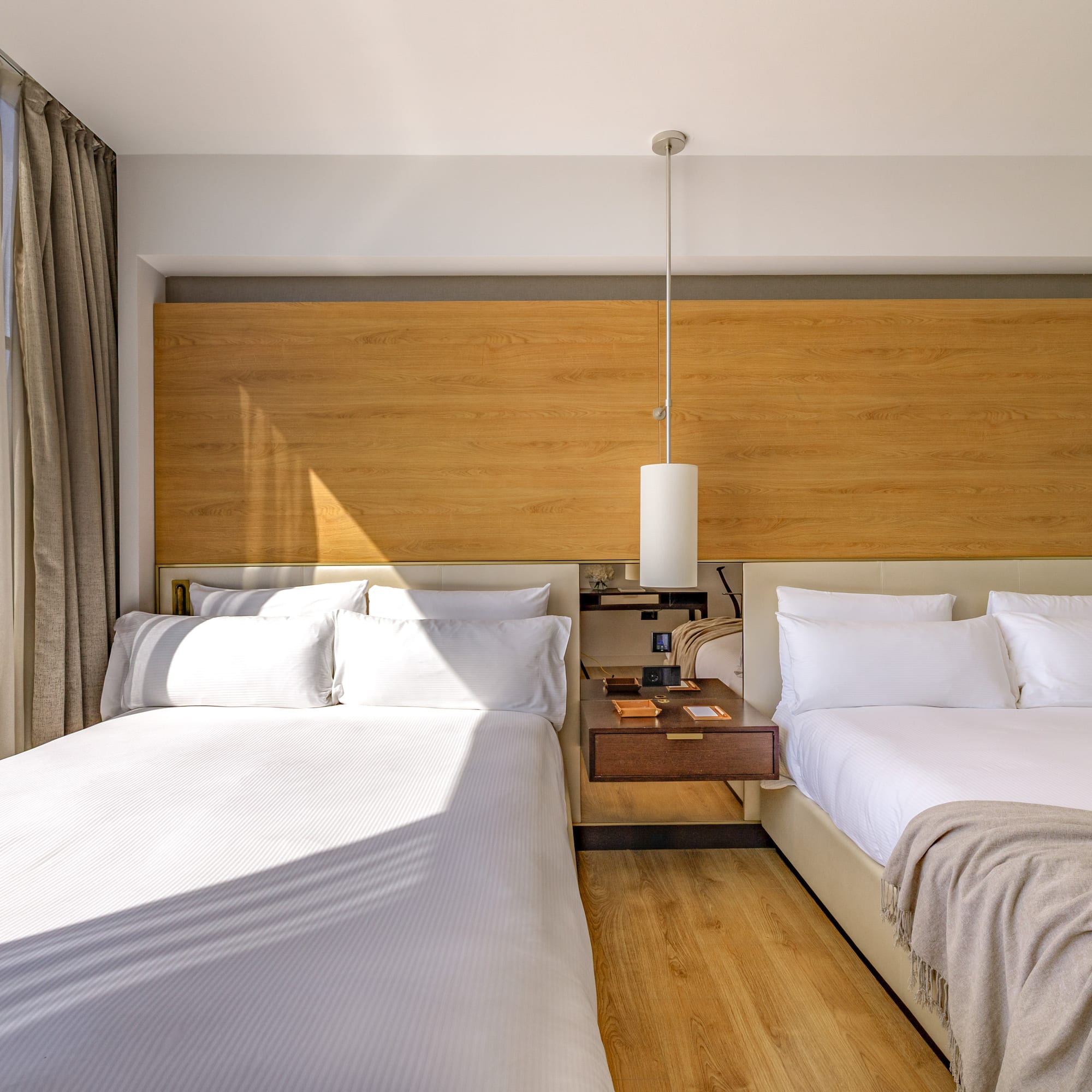 Modern hotel room with two beds, wooden headboard, and scenic mountain view.