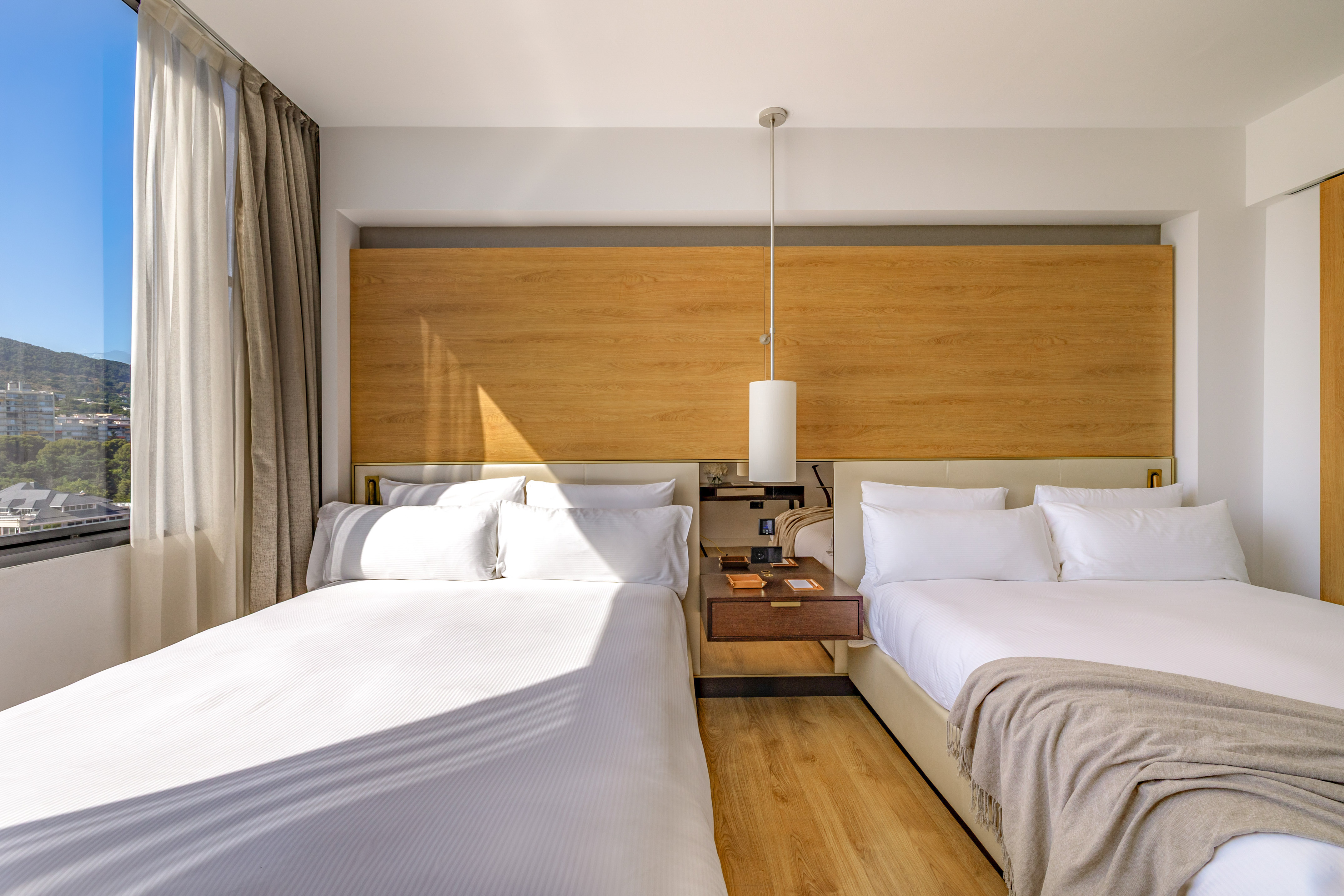 Modern hotel room with two beds, wooden headboard, and scenic mountain view.