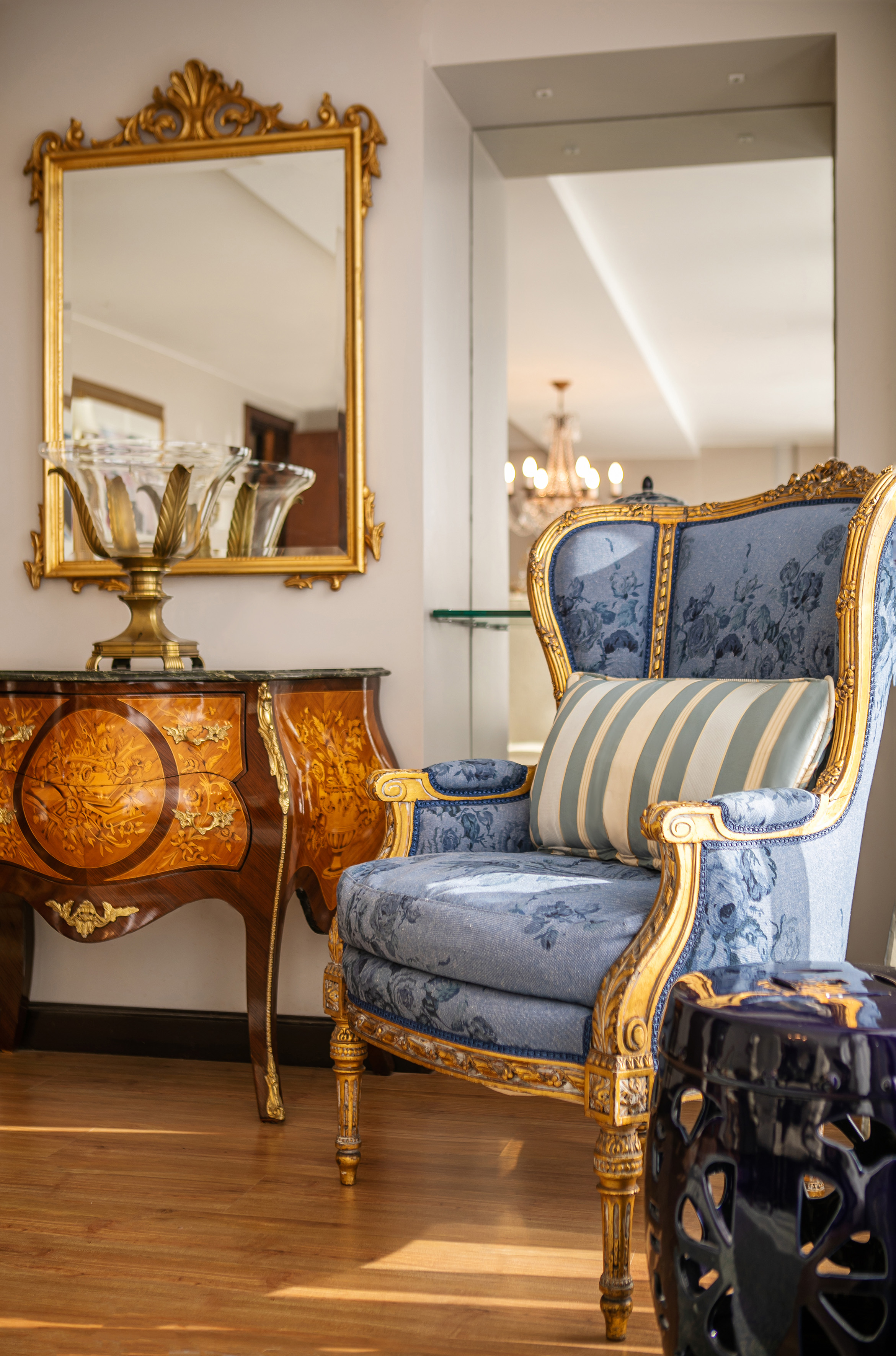 Ornate blue armchair, gold mirror, and marquetry console table in a luxury interior.