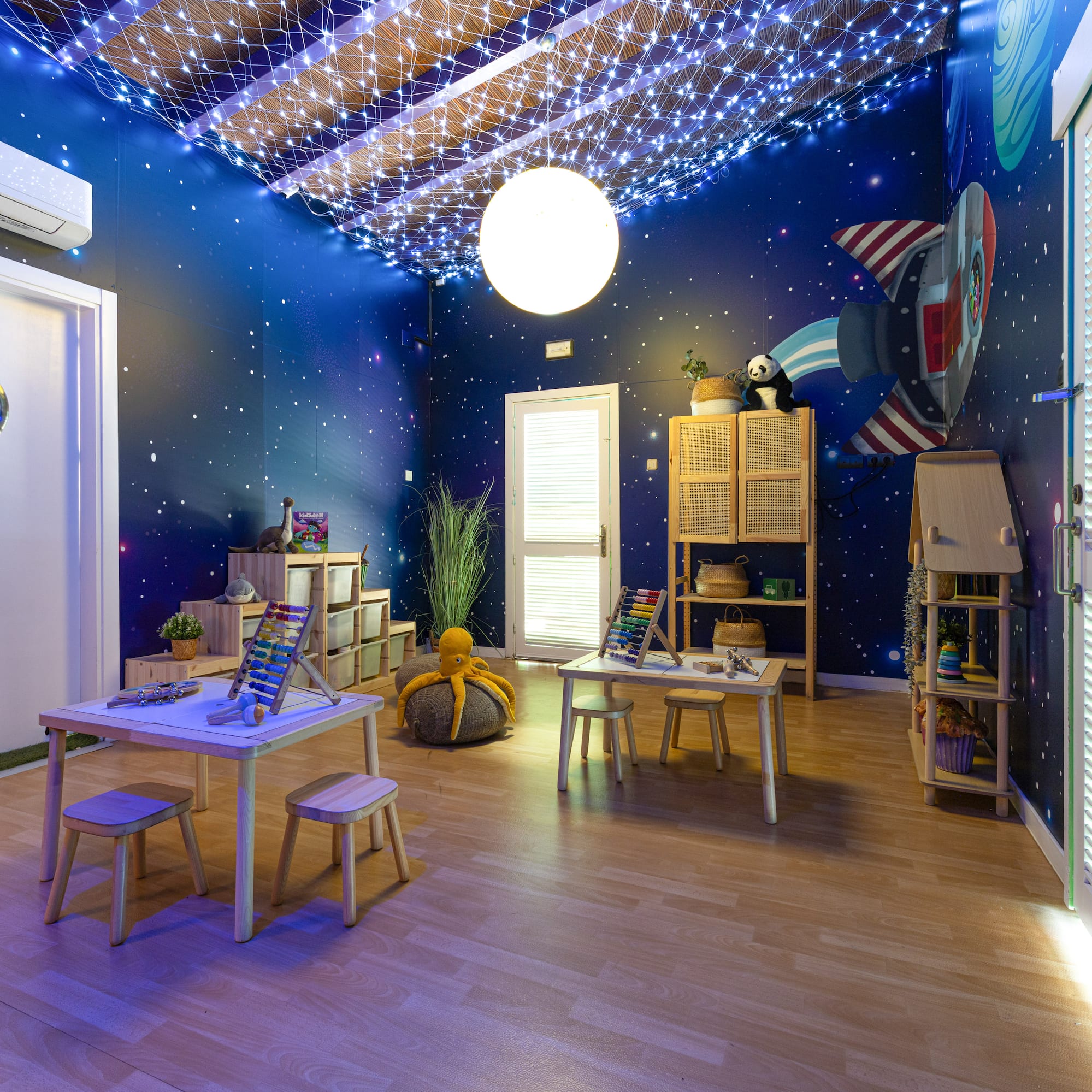 Kids' space-themed playroom with starry walls, rocket mural, and learning tables.