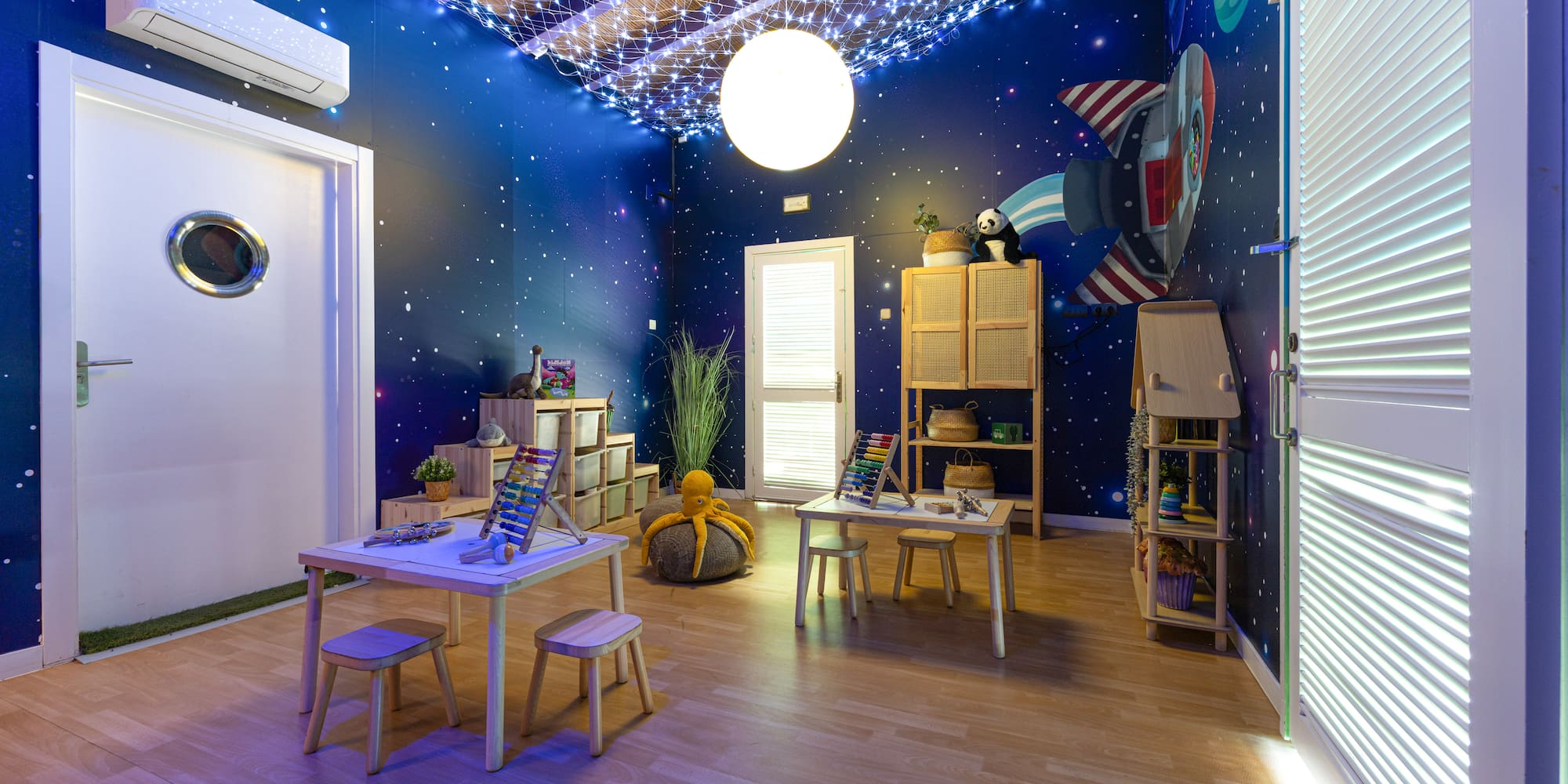Kids' space-themed playroom with starry walls, rocket mural, and learning tables.