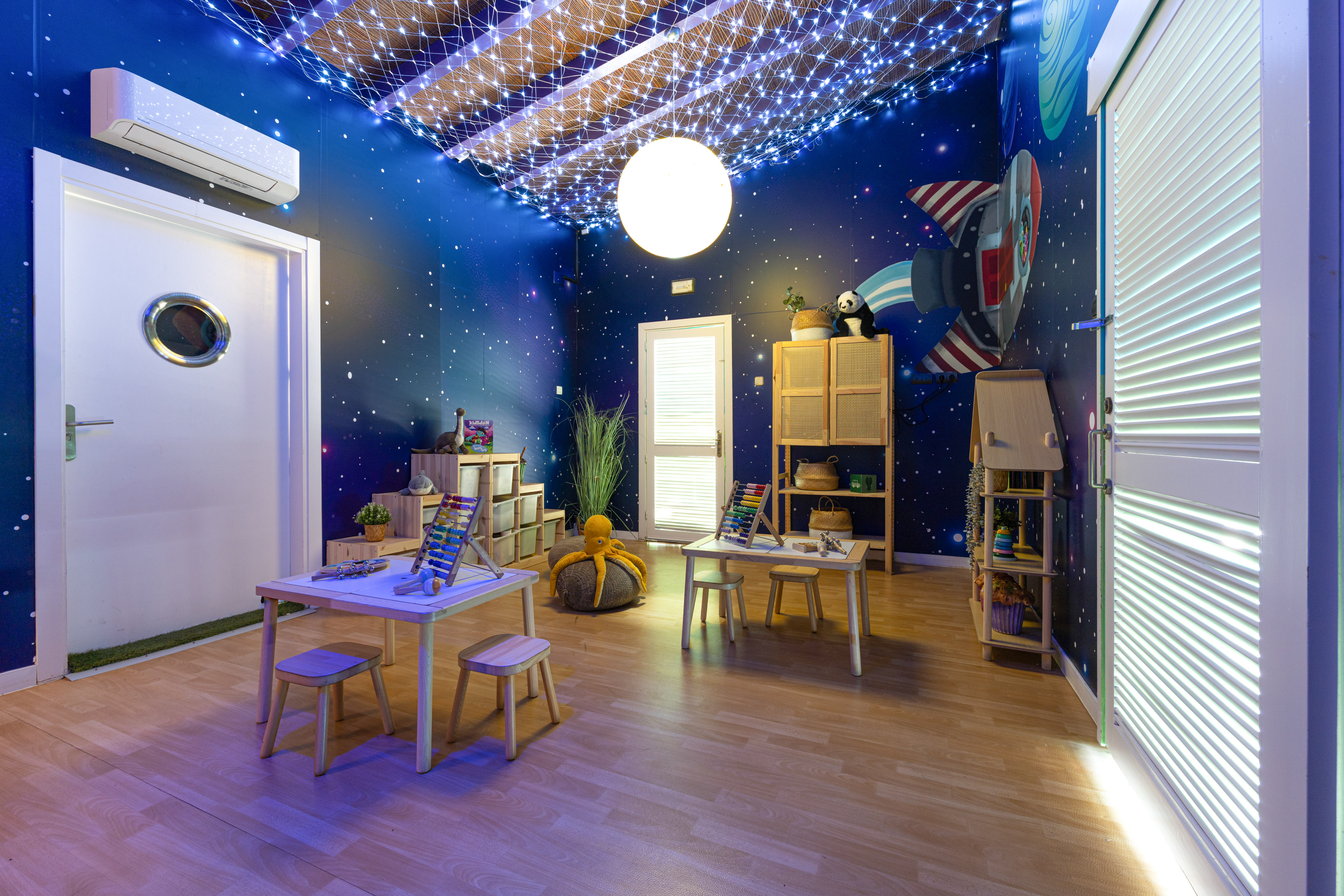 Kids' space-themed playroom with starry walls, rocket mural, and learning tables.