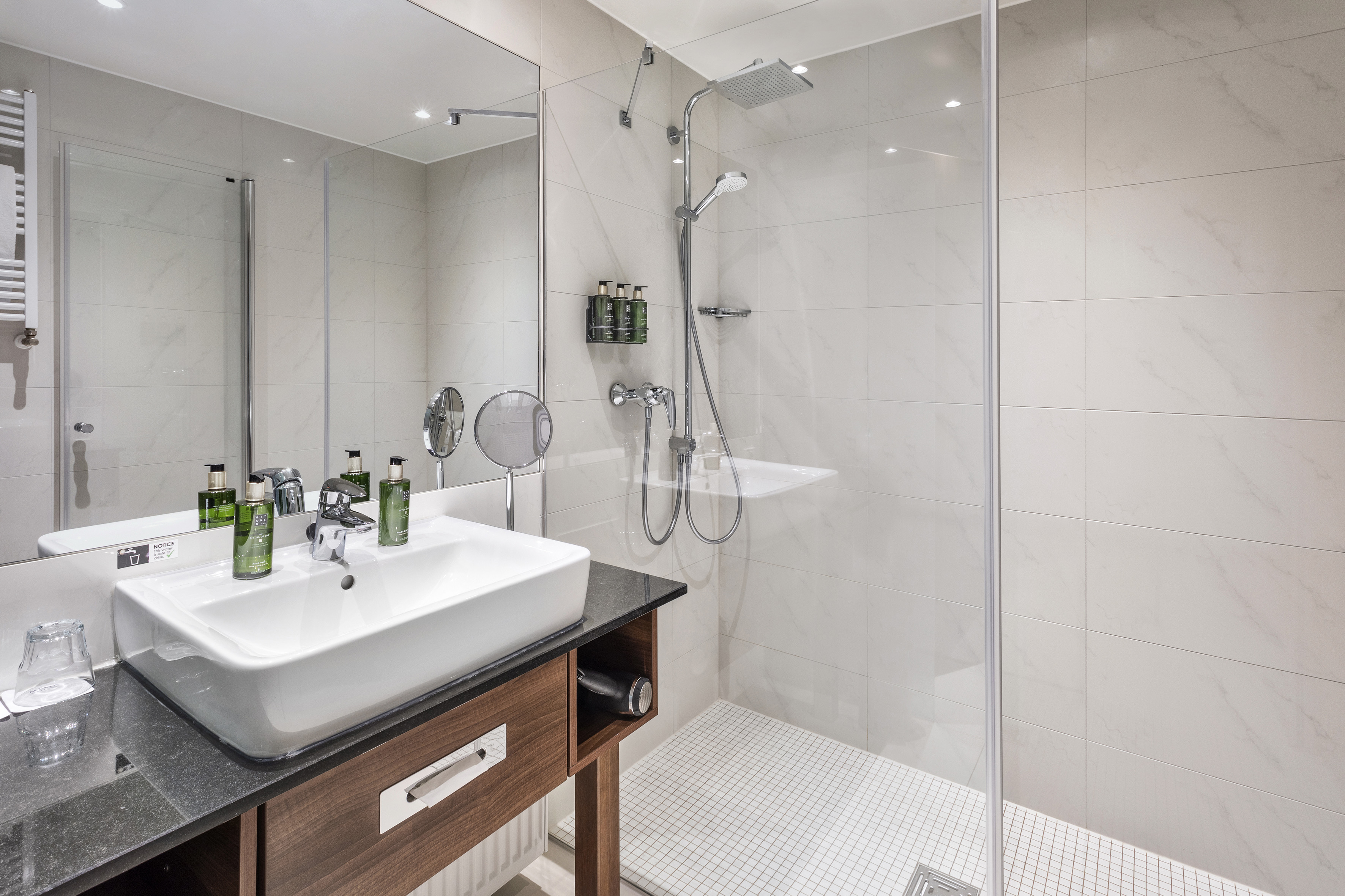 Sleek hotel bathroom with walk-in shower, white sink, and wooden vanity.