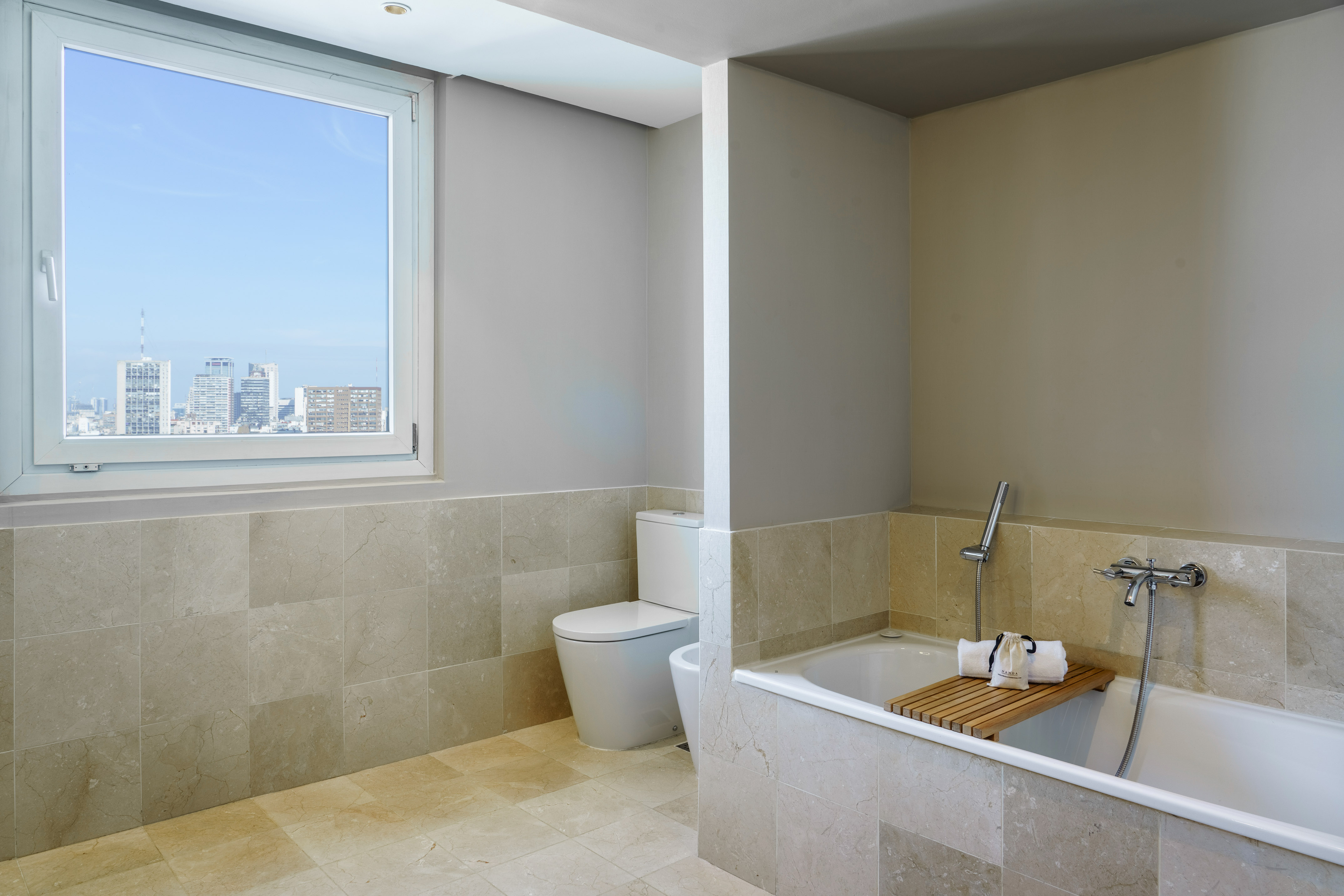 Modern bathroom with city skyline view, bathtub, toilet, and stone tiles.