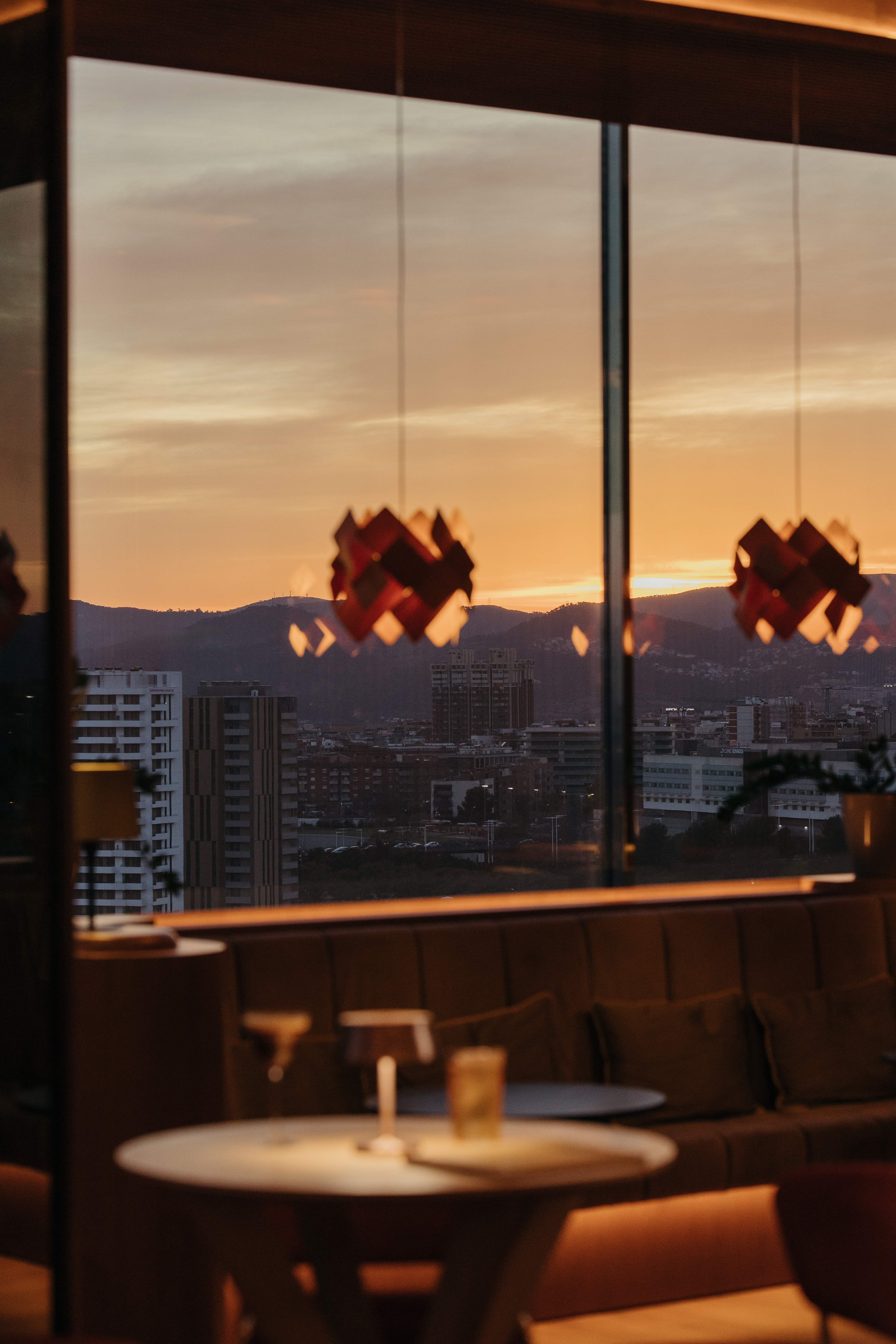 Bar con vistas al atardecer sobre la ciudad y sierra, mesas con copas.