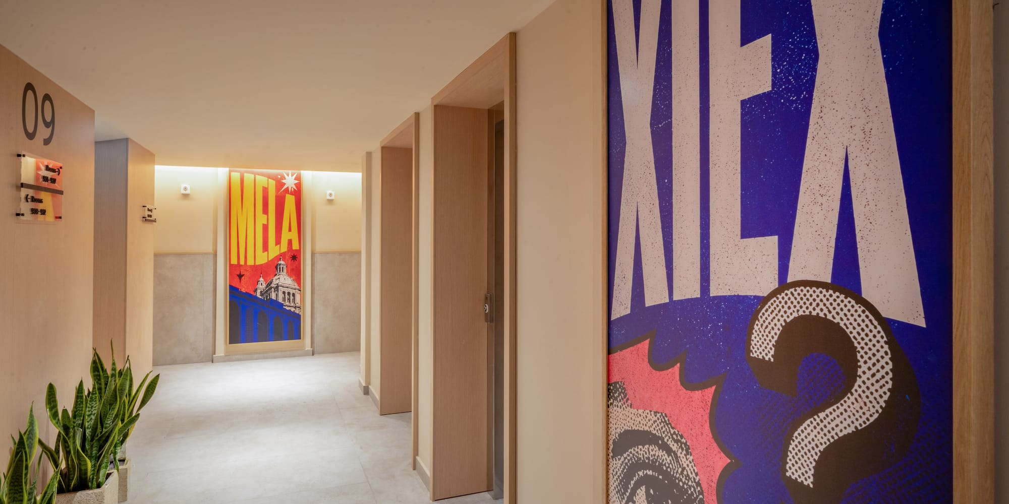Modern hallway with bold pop art posters, wooden doors, and potted plants.