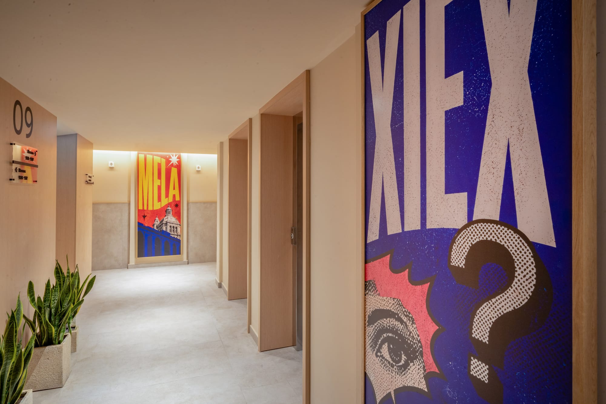 Modern hallway with bold pop art posters, wooden doors, and potted plants.