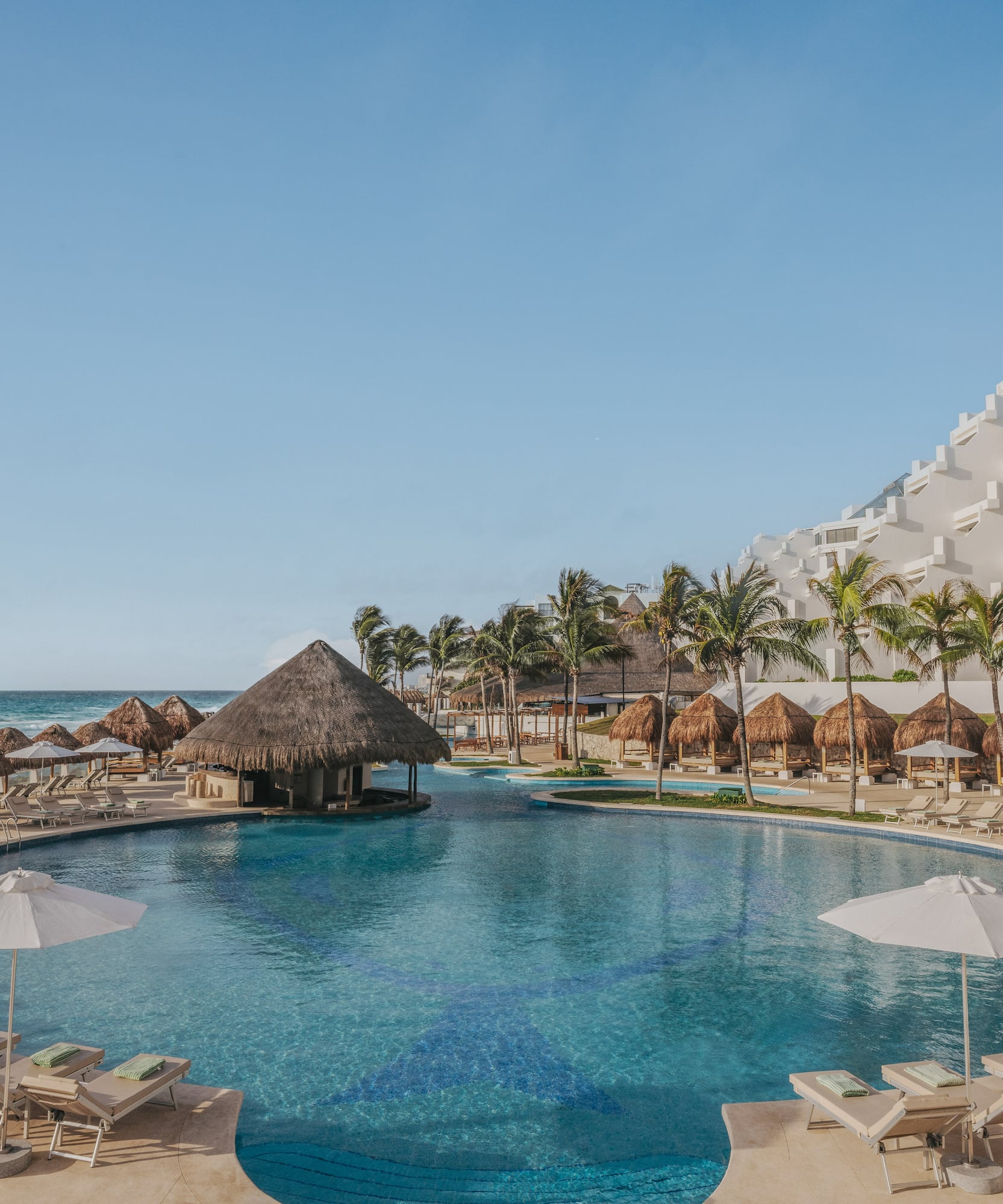 Oceanfront resort pool with swim-up bar, palm trees, white hotel.