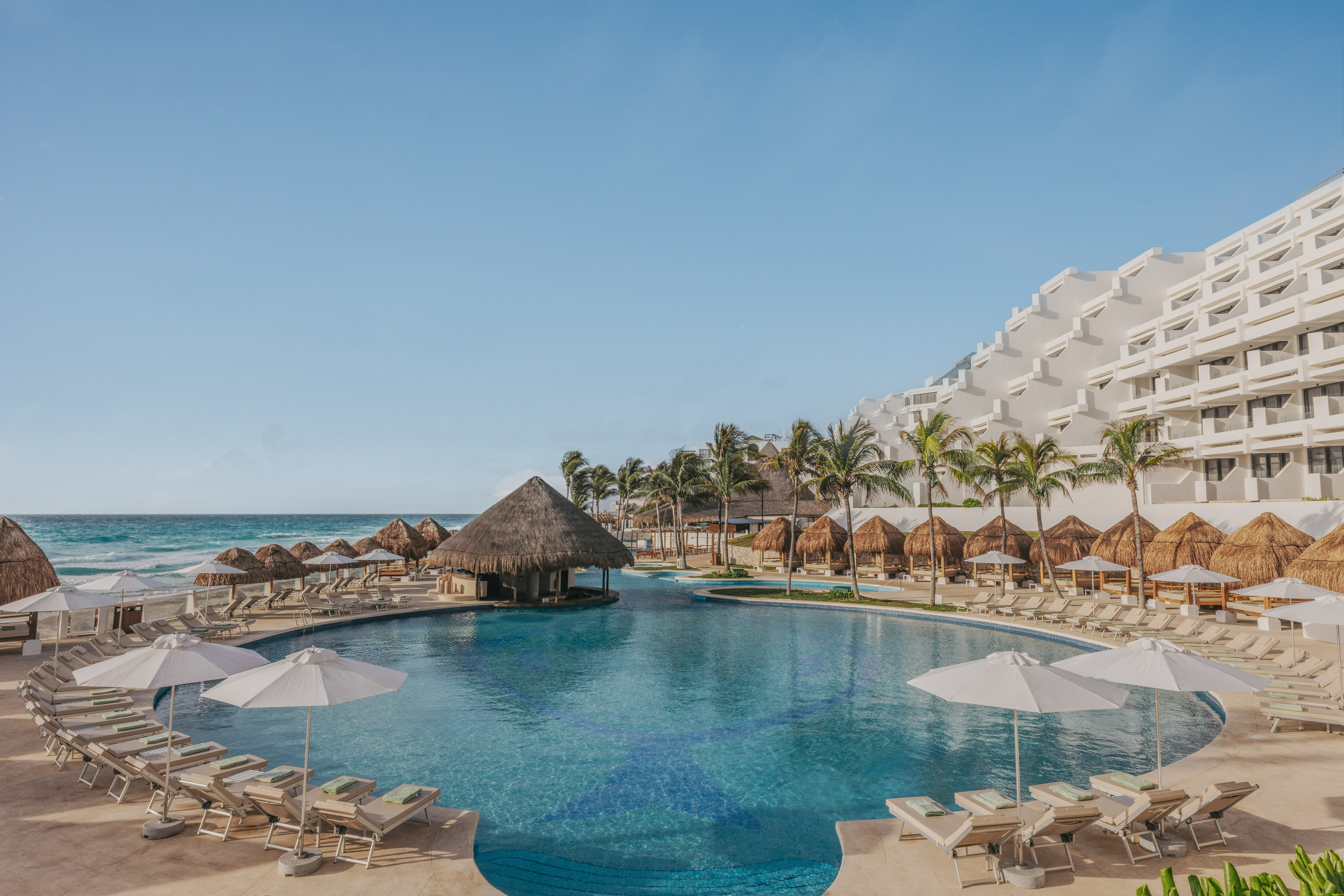 Beachfront resort pool with swim-up bar, palm trees, lounge chairs, and hotel.