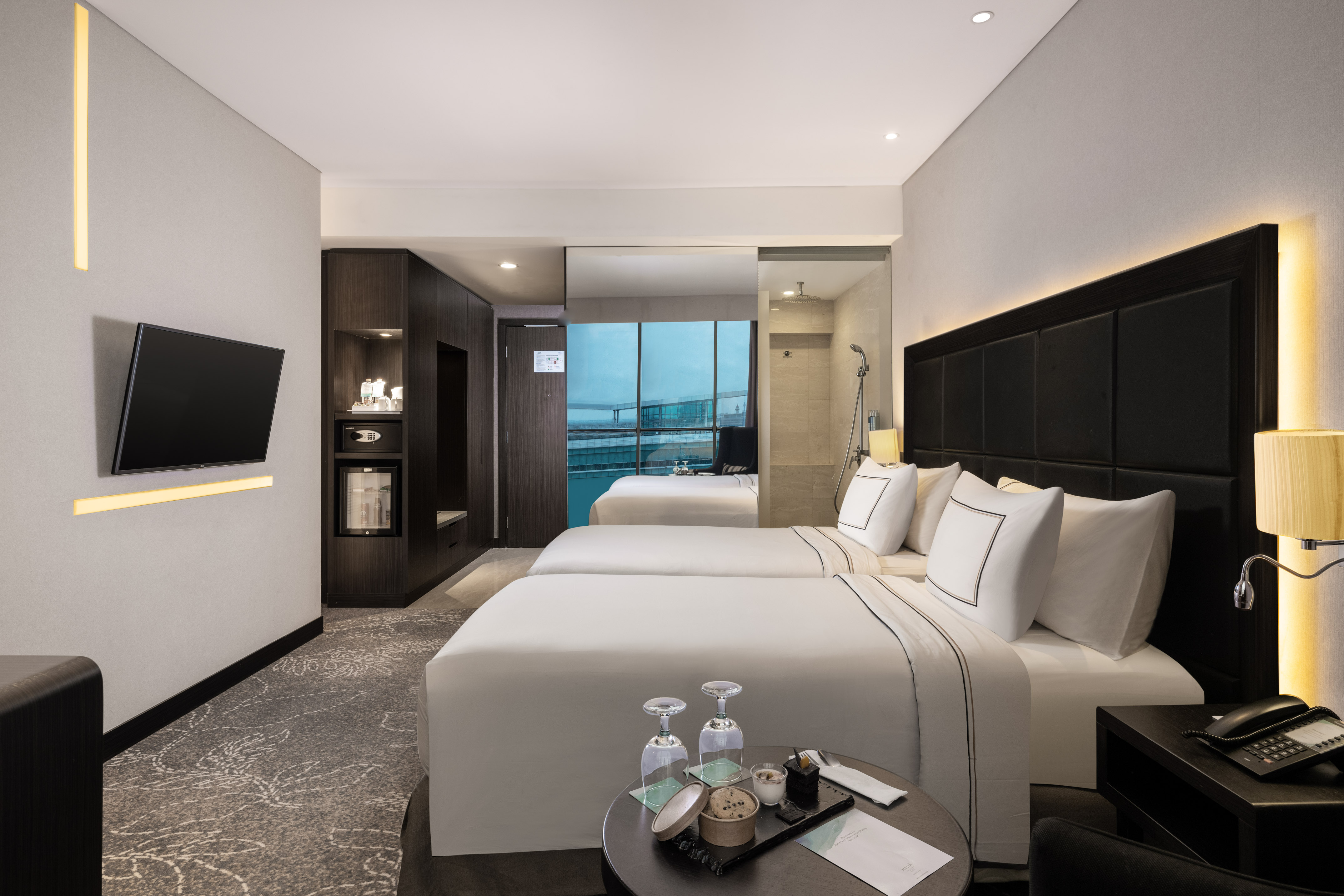 Luxury hotel guest room with twin beds, smart TV, minibar, city view.