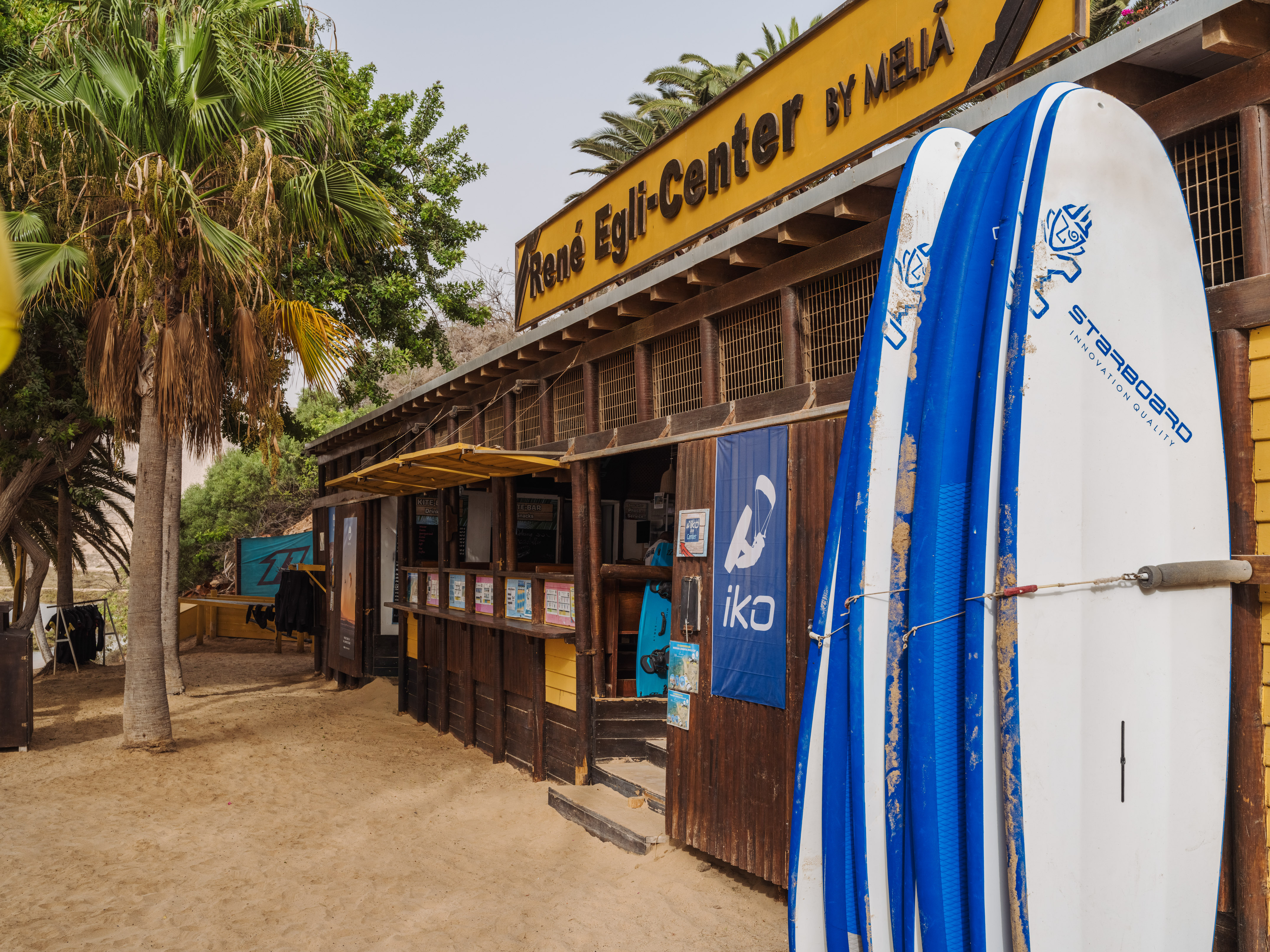 René Egli-Center by Meliá, surf school with boards on a sandy beach.