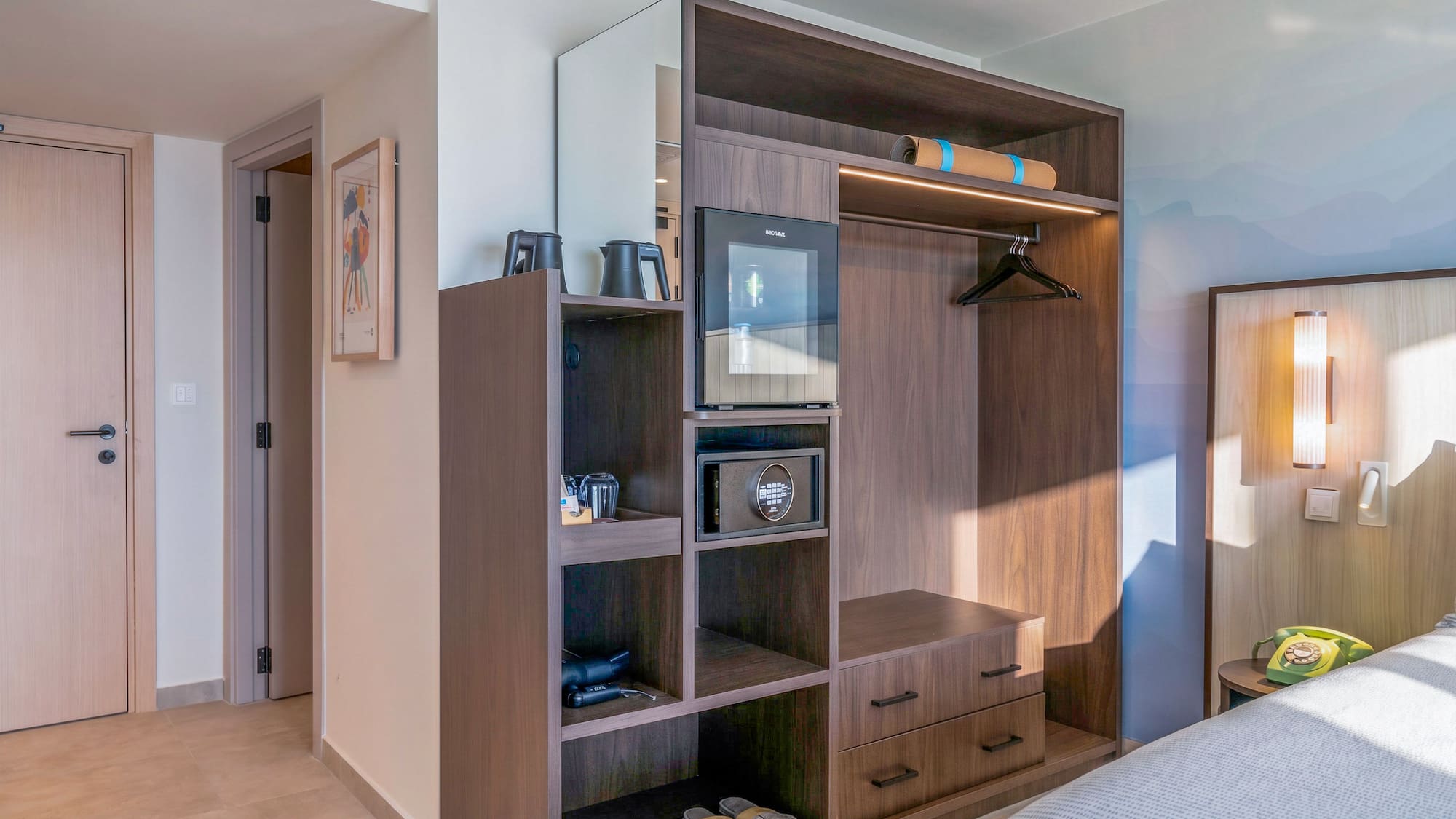 Modern hotel room with built-in dark wood wardrobe, mini-fridge, and safe.
