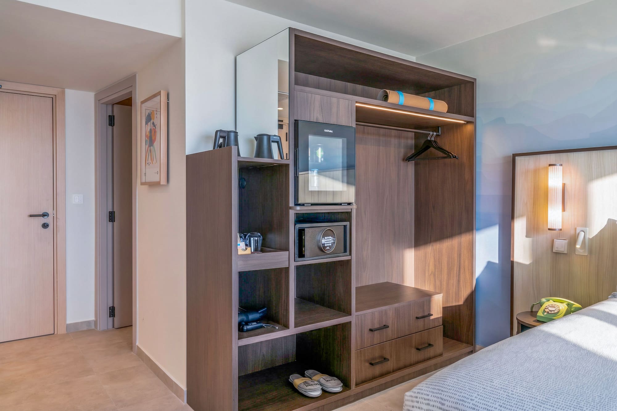 Modern hotel room with built-in dark wood wardrobe, mini-fridge, and safe.