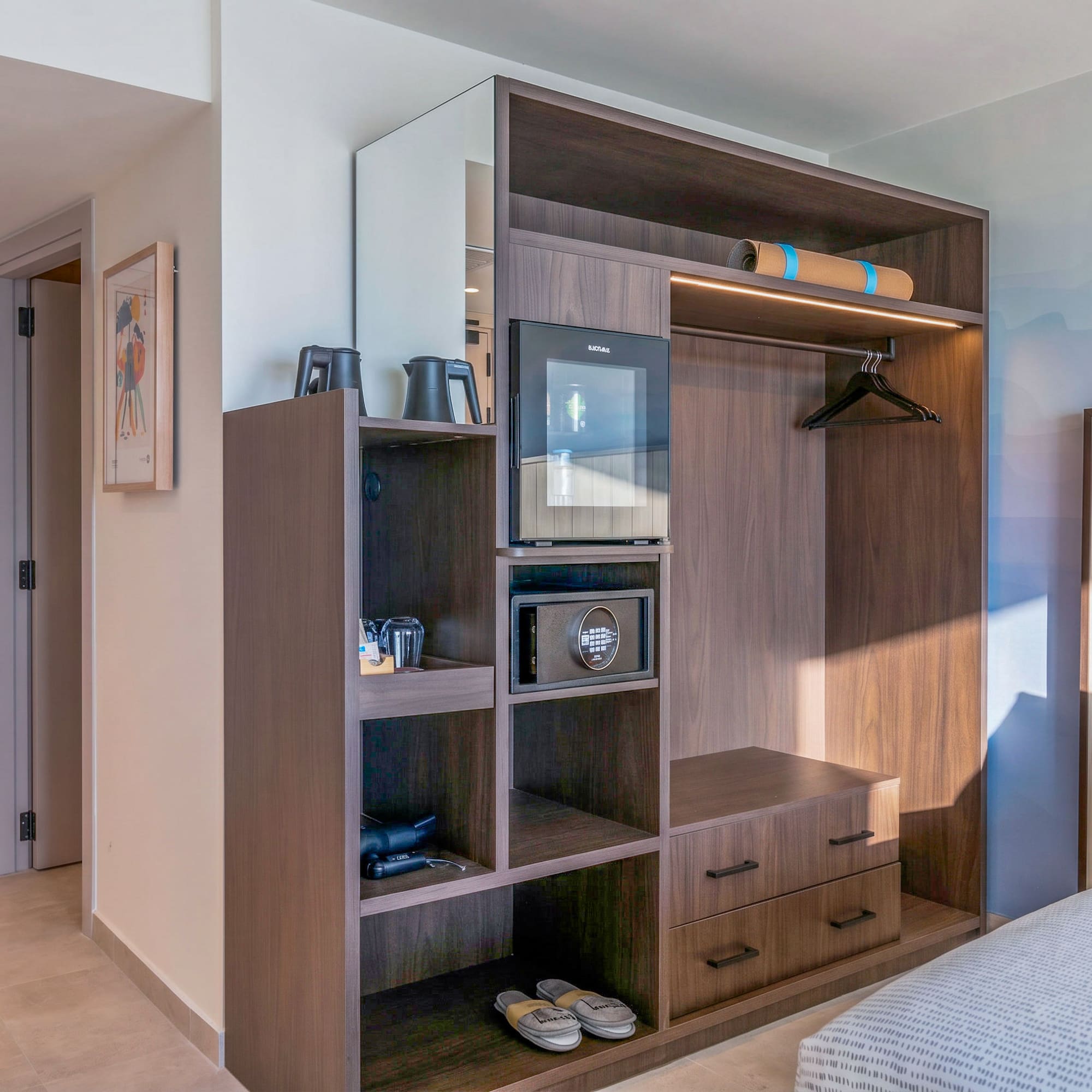 Modern hotel room with built-in dark wood wardrobe, mini-fridge, and safe.