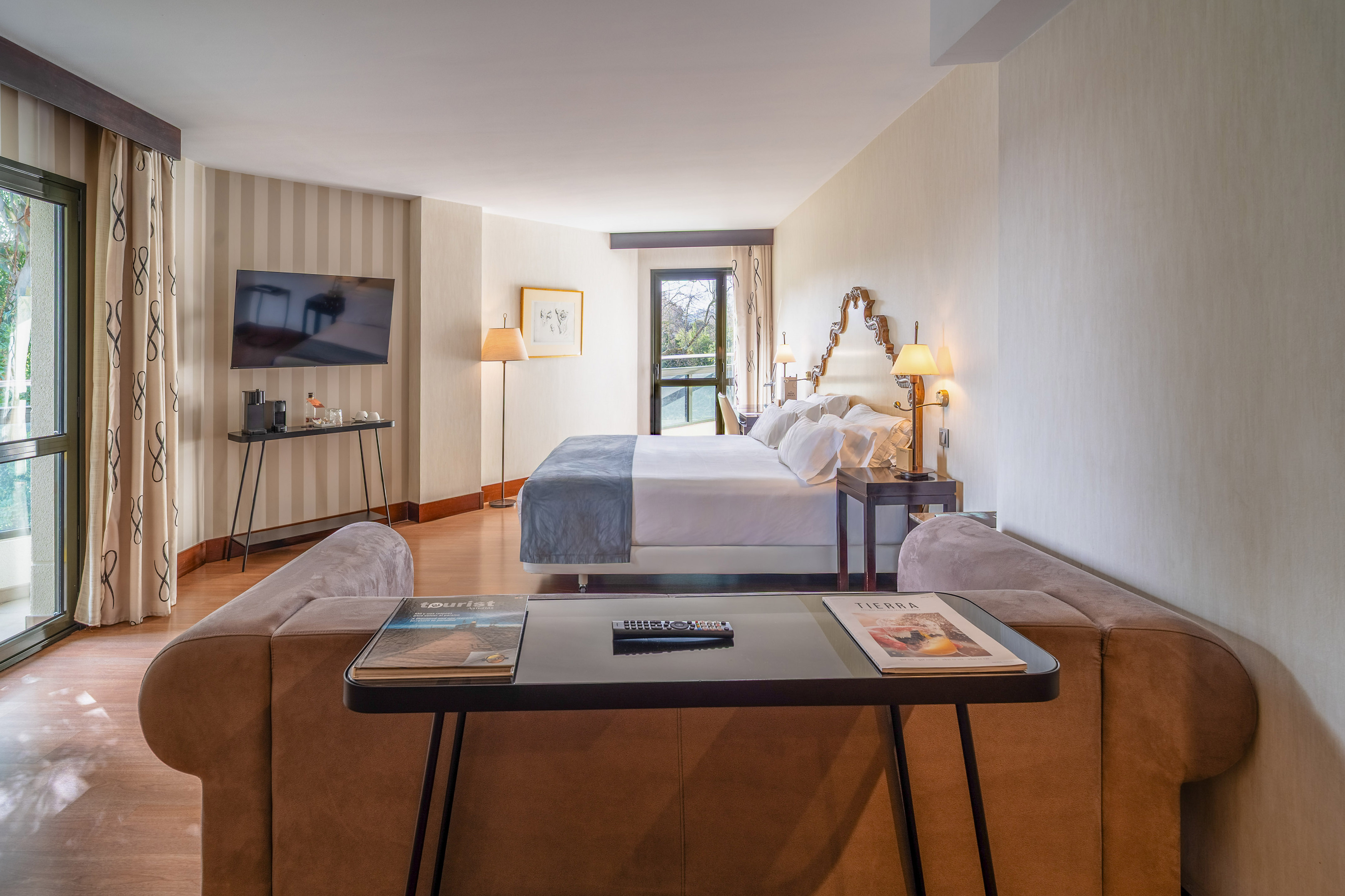 Stylish hotel suite with large bed, sofa, TV, and balcony.