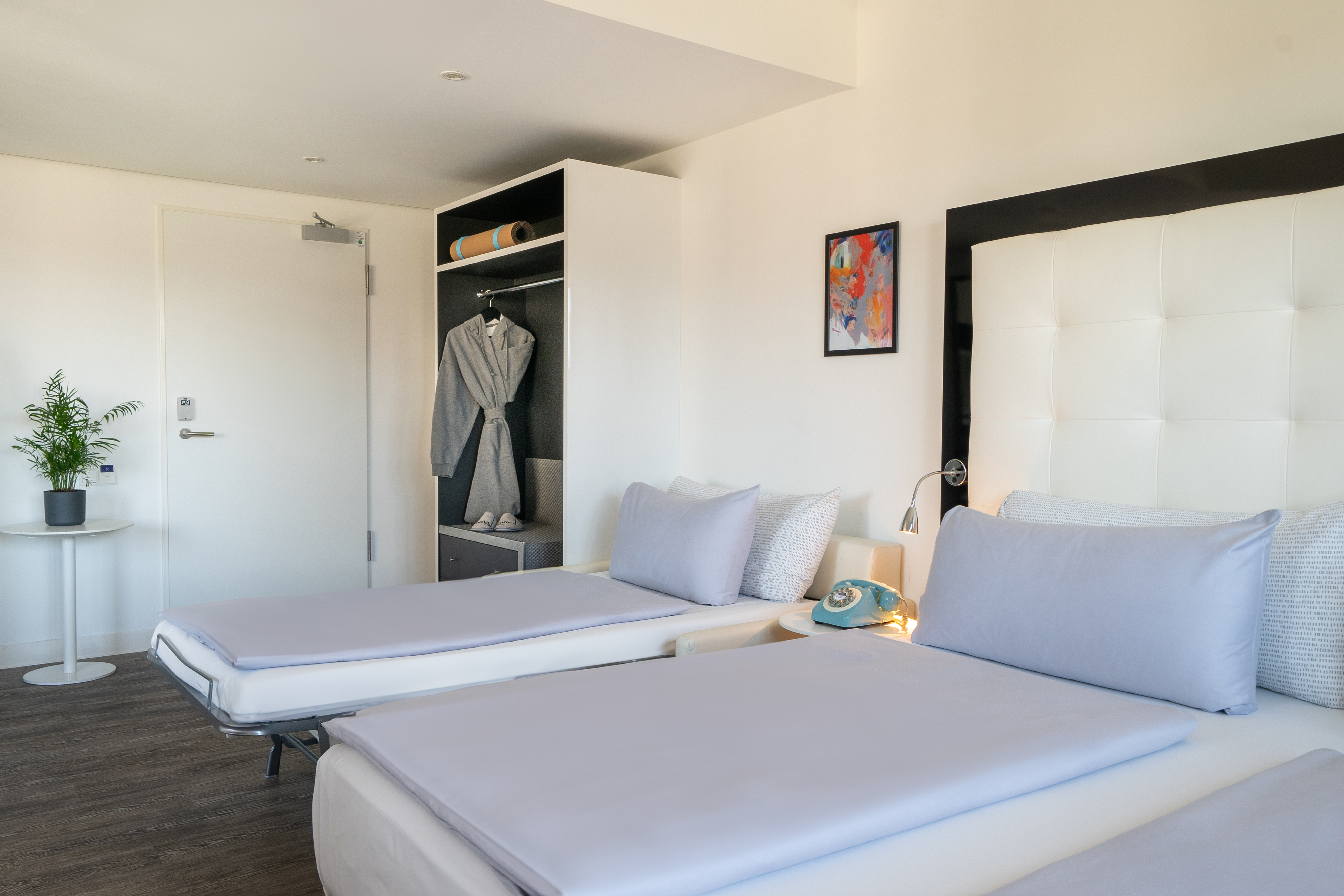Modern hotel room with two twin beds, white headboard, and open wardrobe.