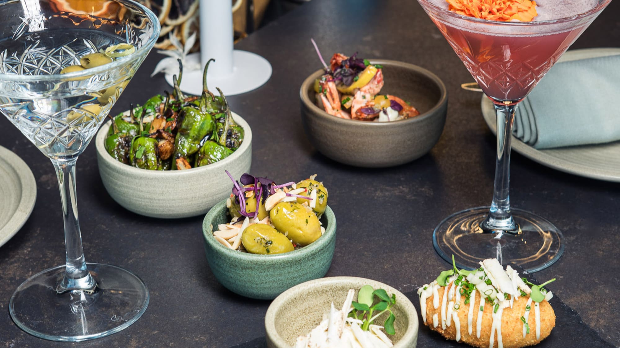 Cocktails, martini, and varied tapas on a dark bar counter.