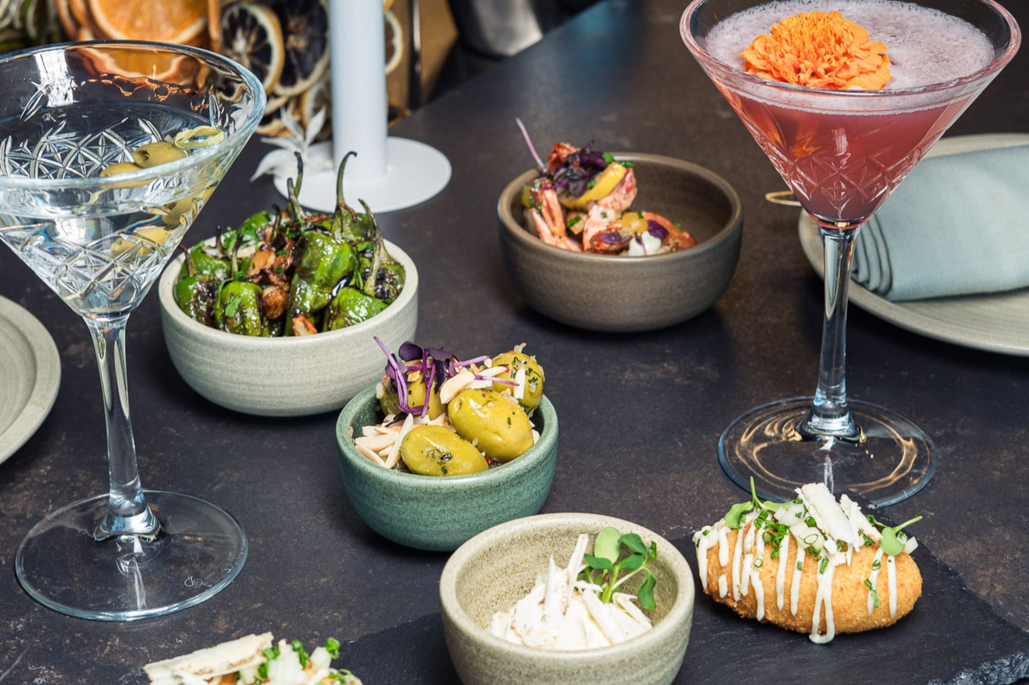 Cocktails, martini, and varied tapas on a dark bar counter.