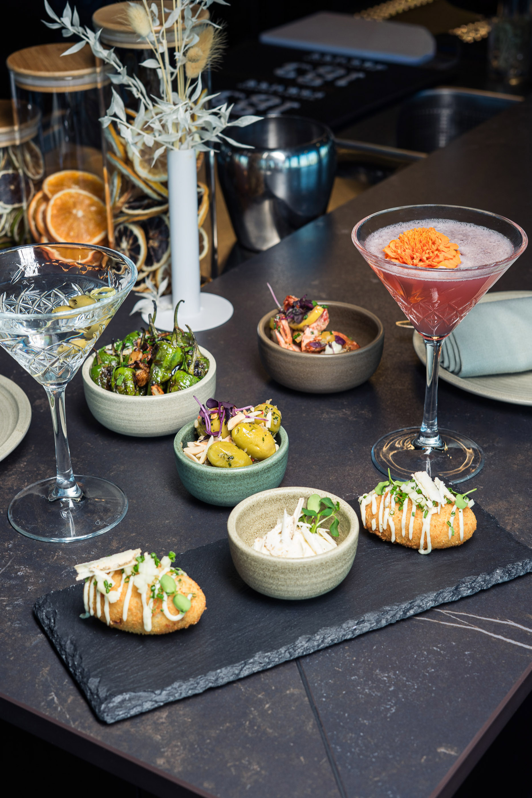 Cocktails, martini, and varied tapas on a dark bar counter.