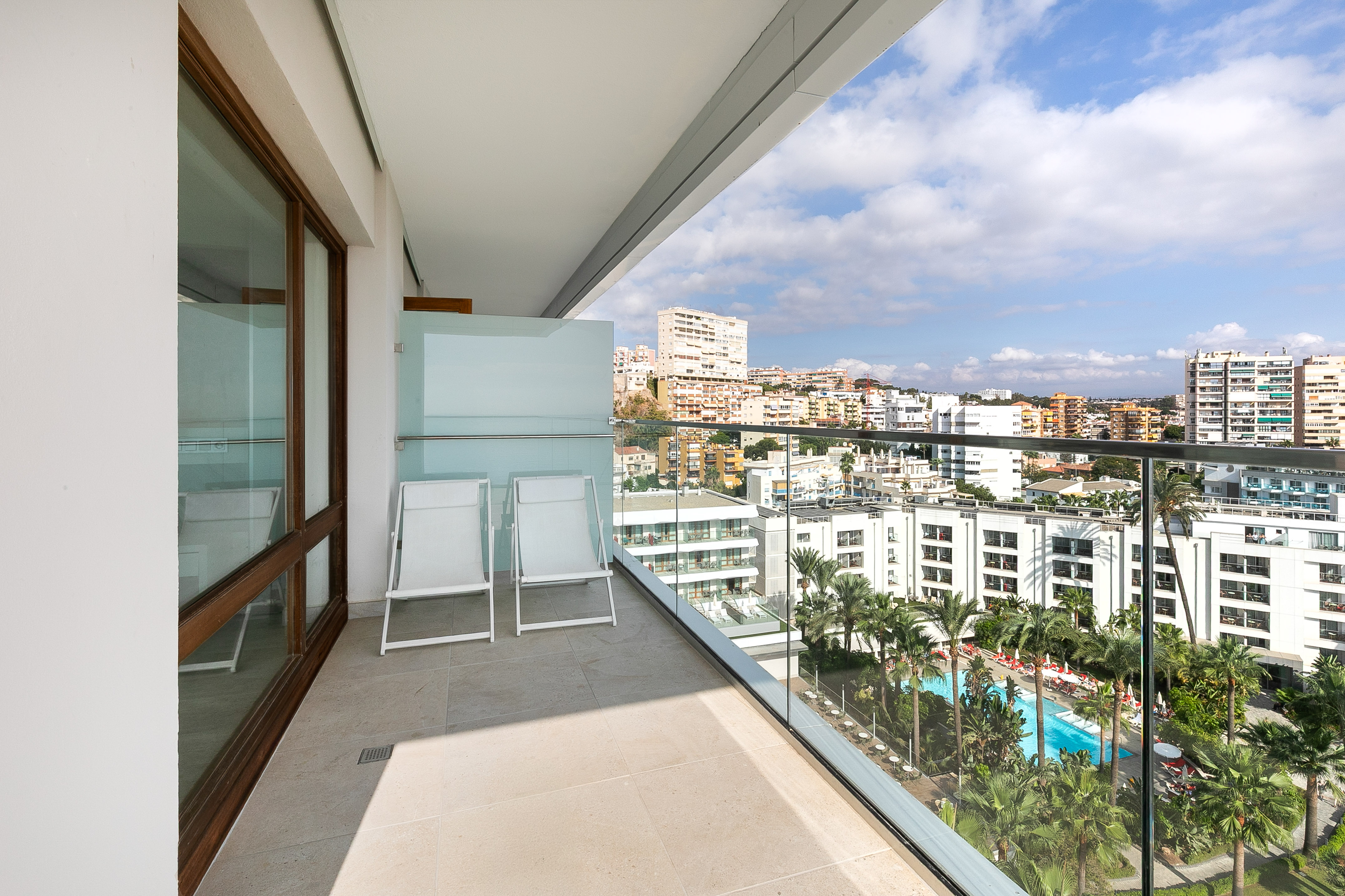 Balcony with city skyline, pool view, and two white lounge chairs.