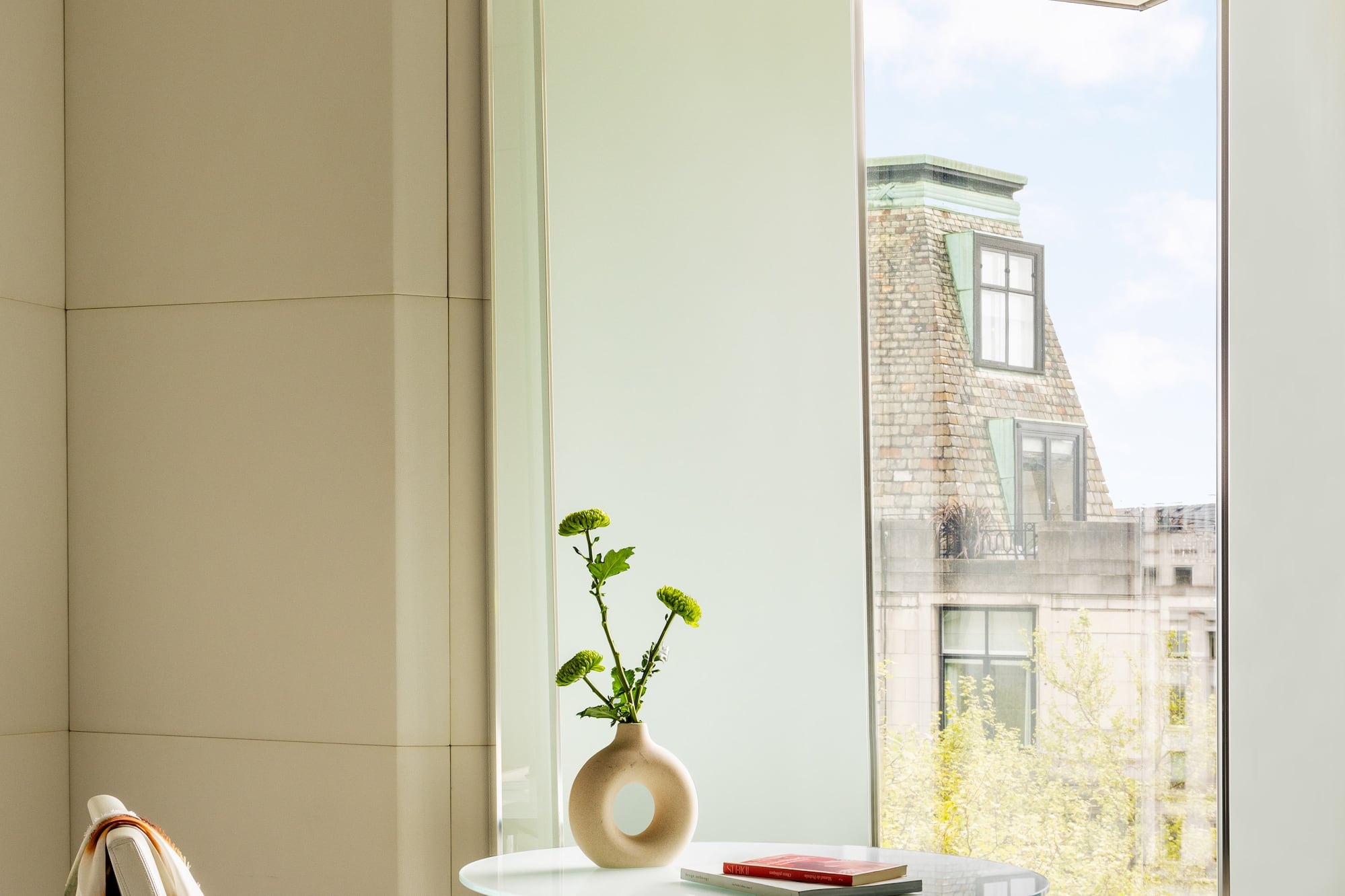 a glass table with a vase on it and a chair by a window