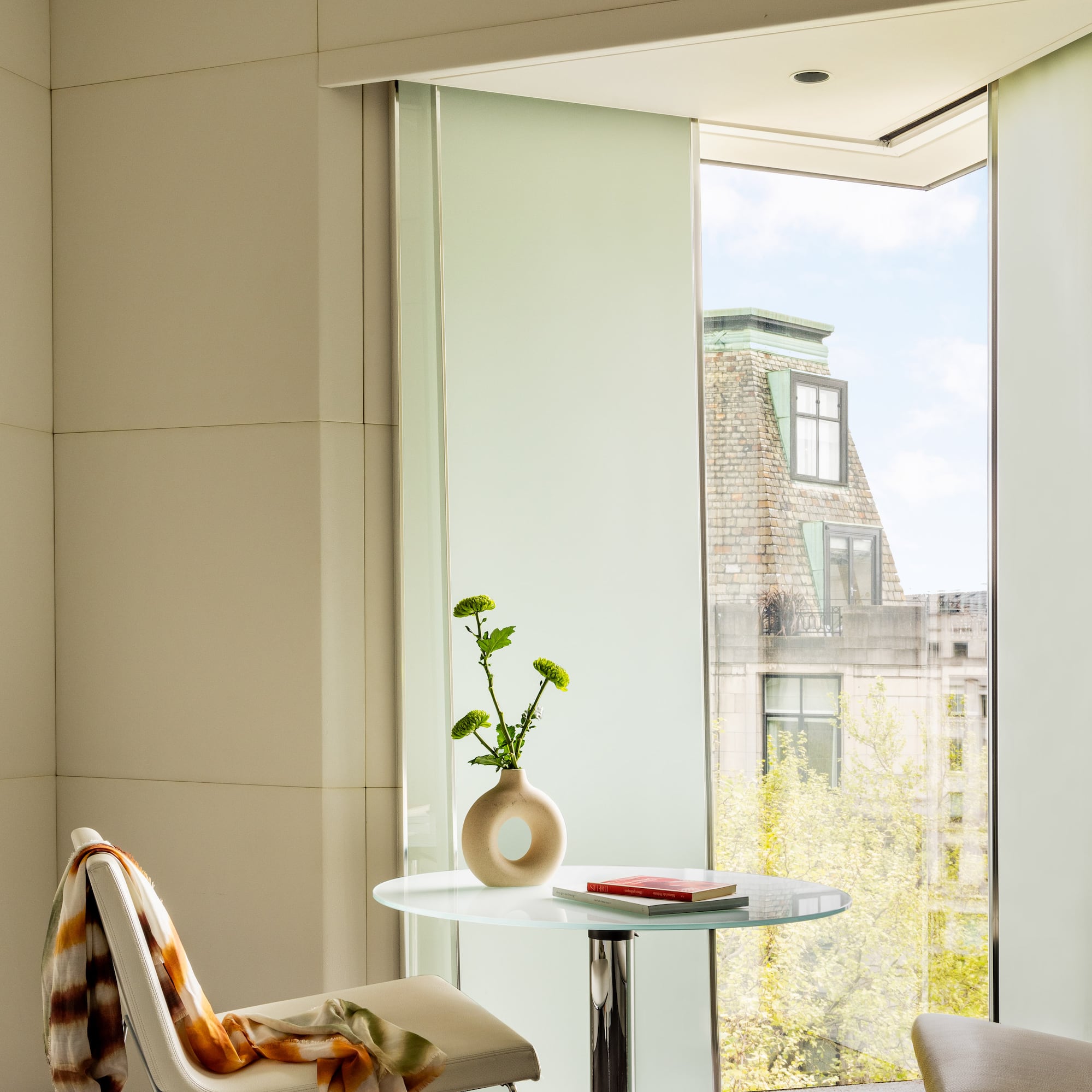 a glass table with a vase on it and a chair by a window
