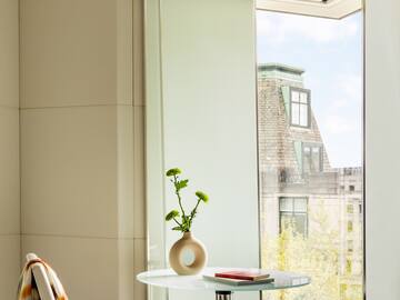 a glass table with a vase on it and a chair by a window