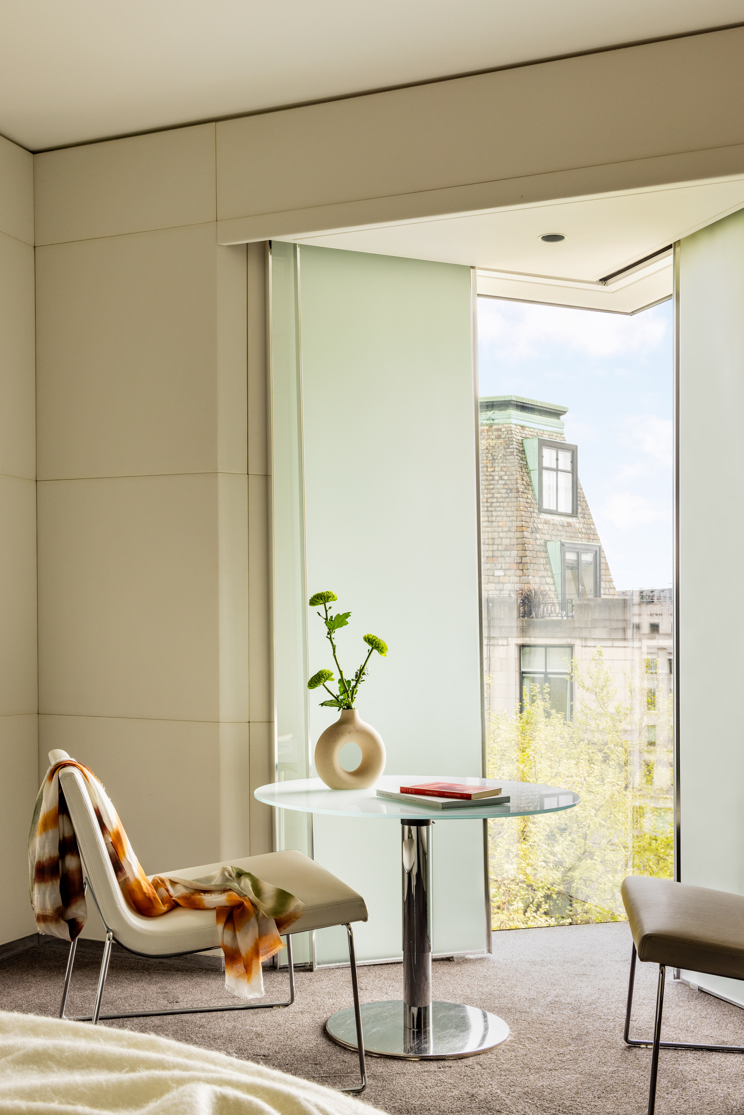 Modern room, glass table with green flowers, sleek chairs, and city view window.