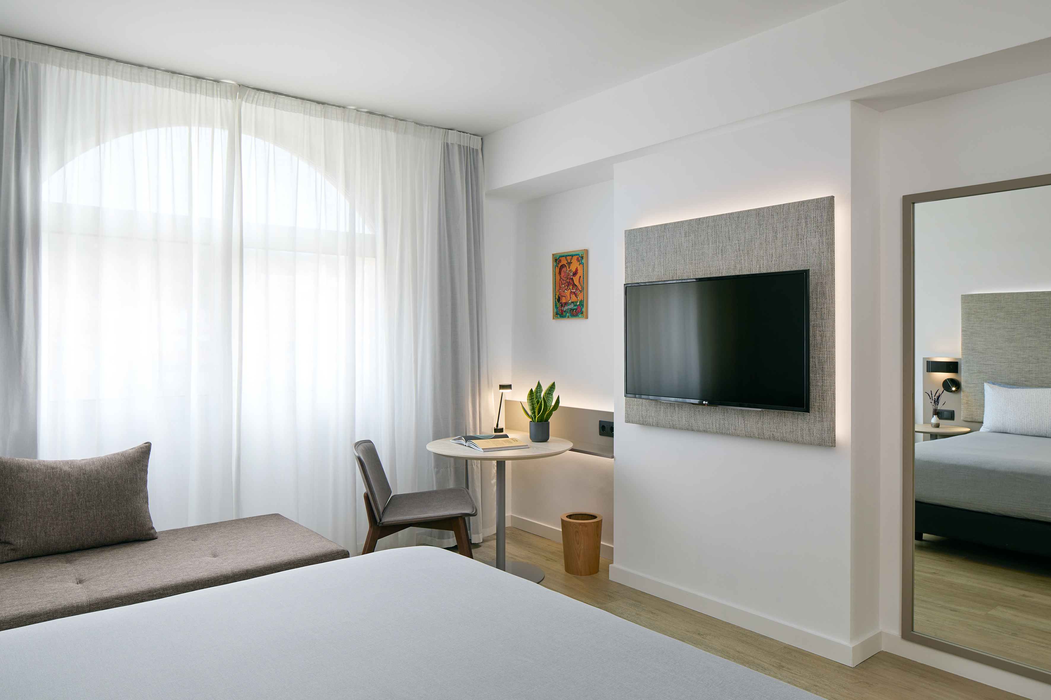 Comfortable hotel room with bed, desk, TV, and sheer-curtained arched window.