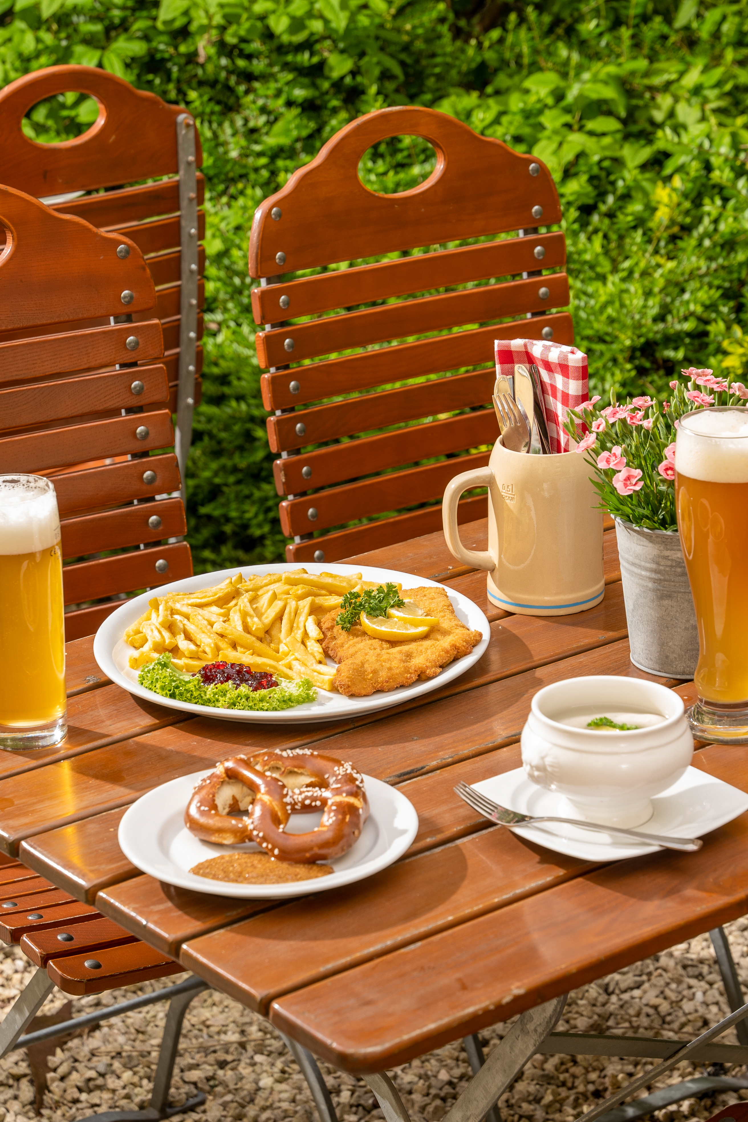 German Wiener Schnitzel, fries, pretzel, and beer on an outdoor table.