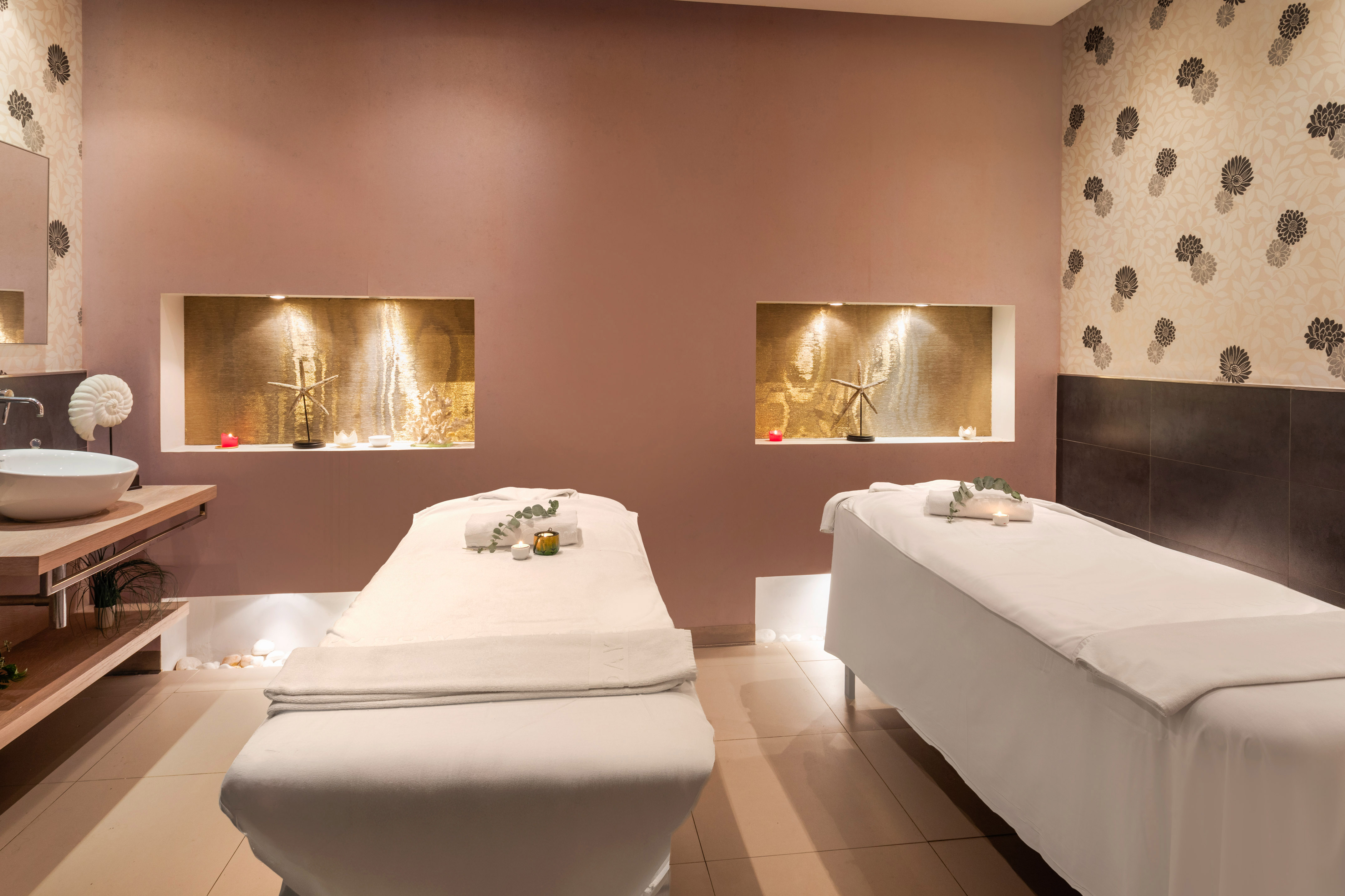 Luxurious spa massage room with two treatment beds and warm decorative lighting.