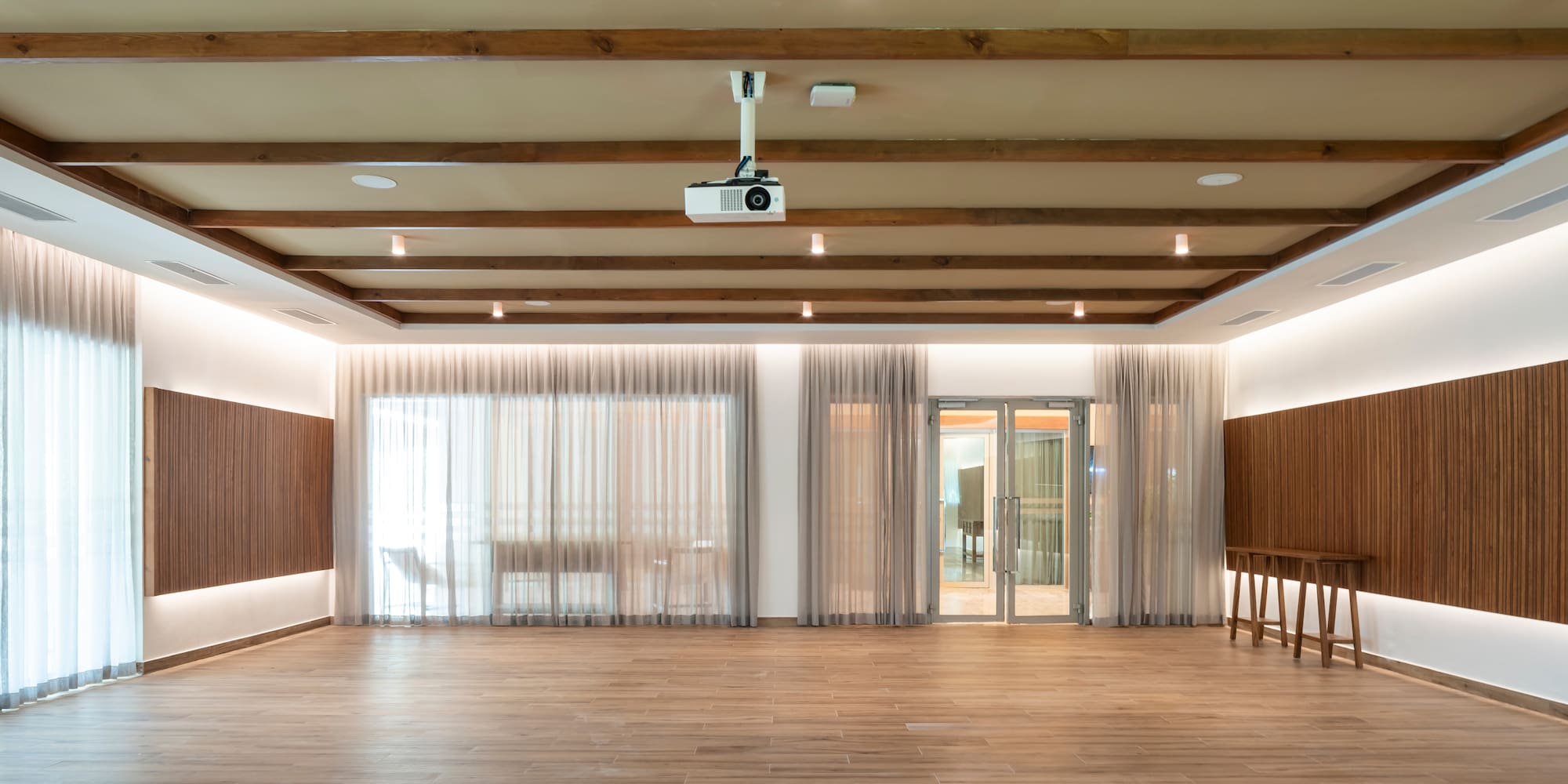 Empty modern event space with wood floor, ceiling beams, projector.