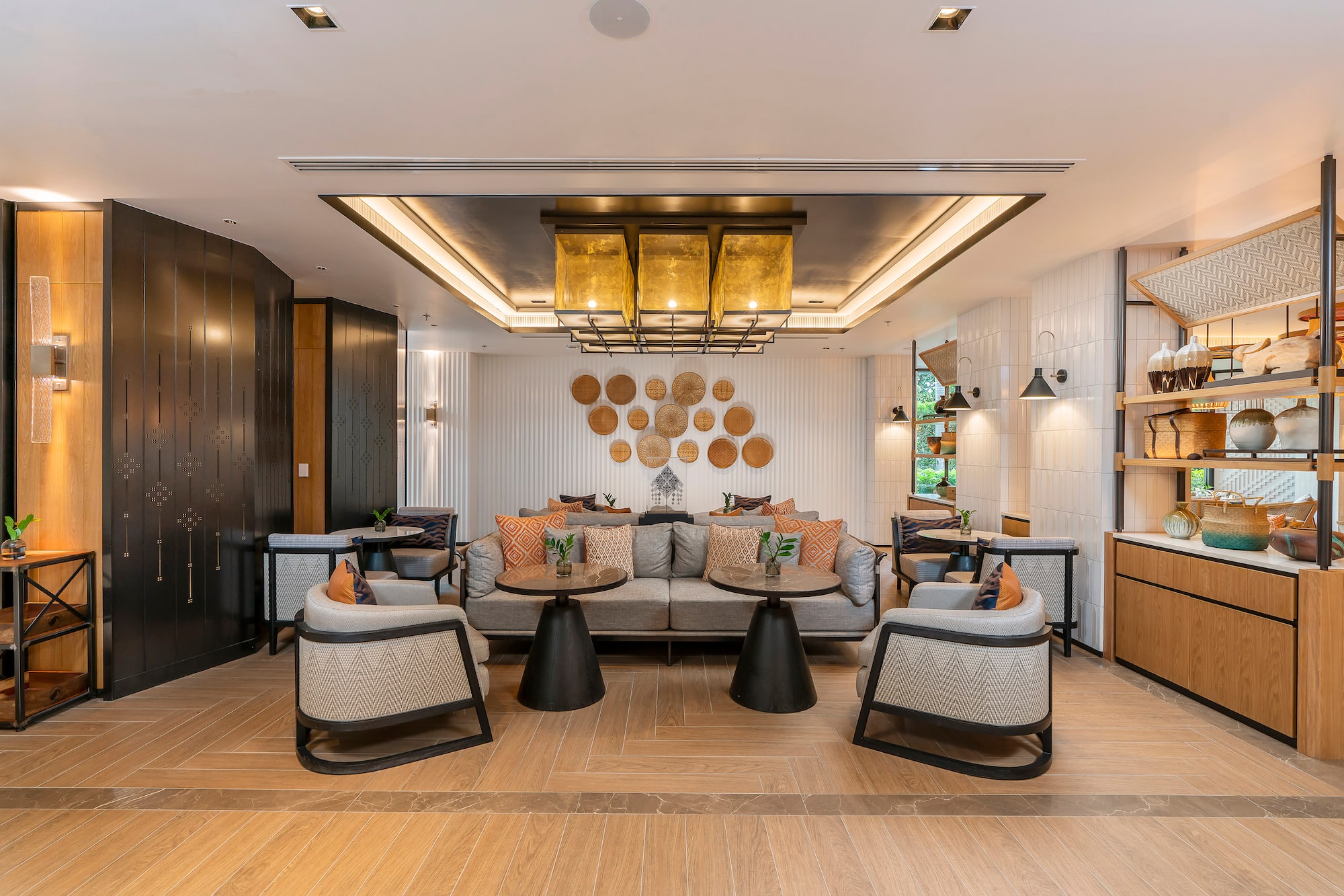 Modern hotel lounge with cozy seating, woven wall art, and gold chandelier.