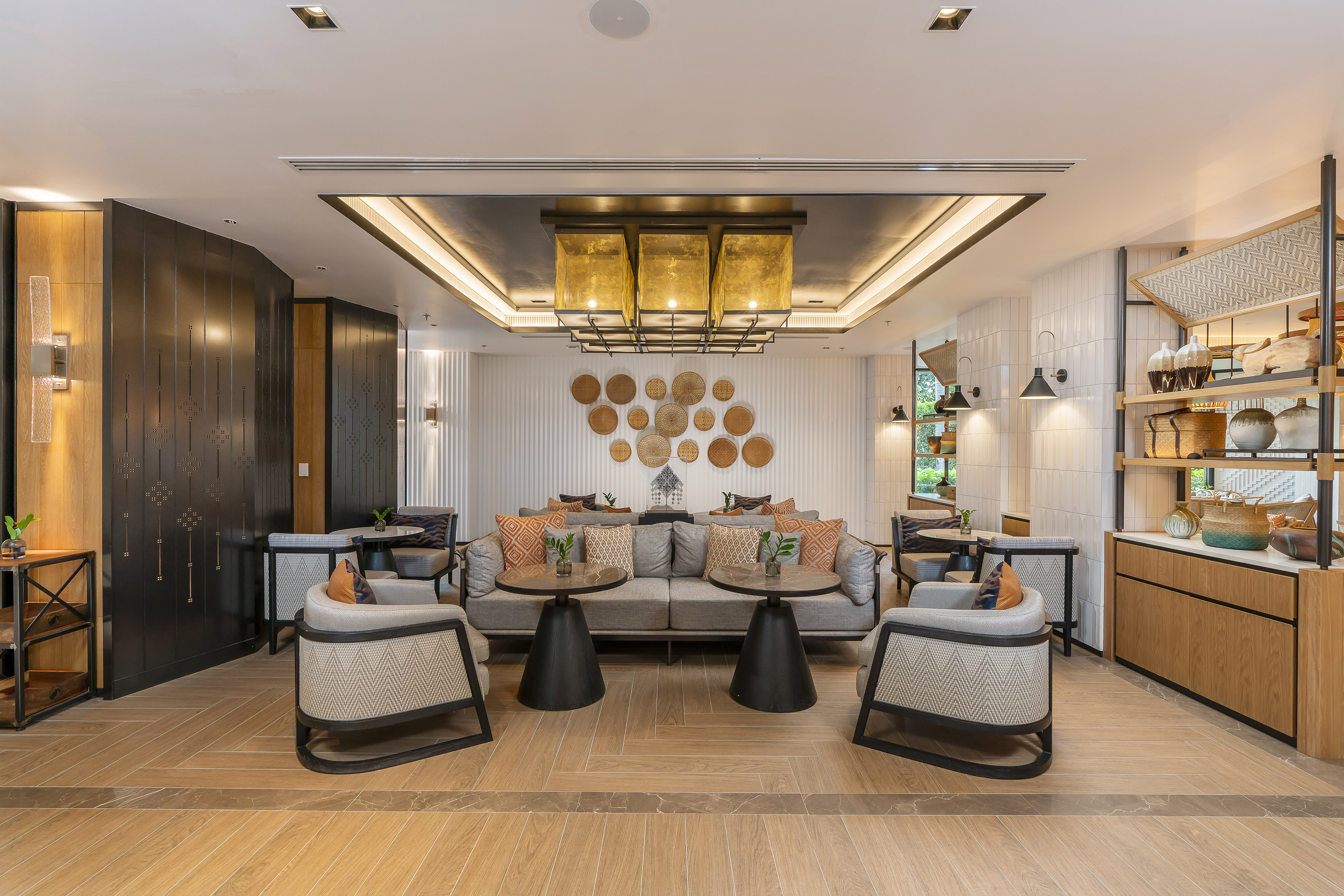 Modern hotel lounge with cozy seating, woven wall art, and gold chandelier.