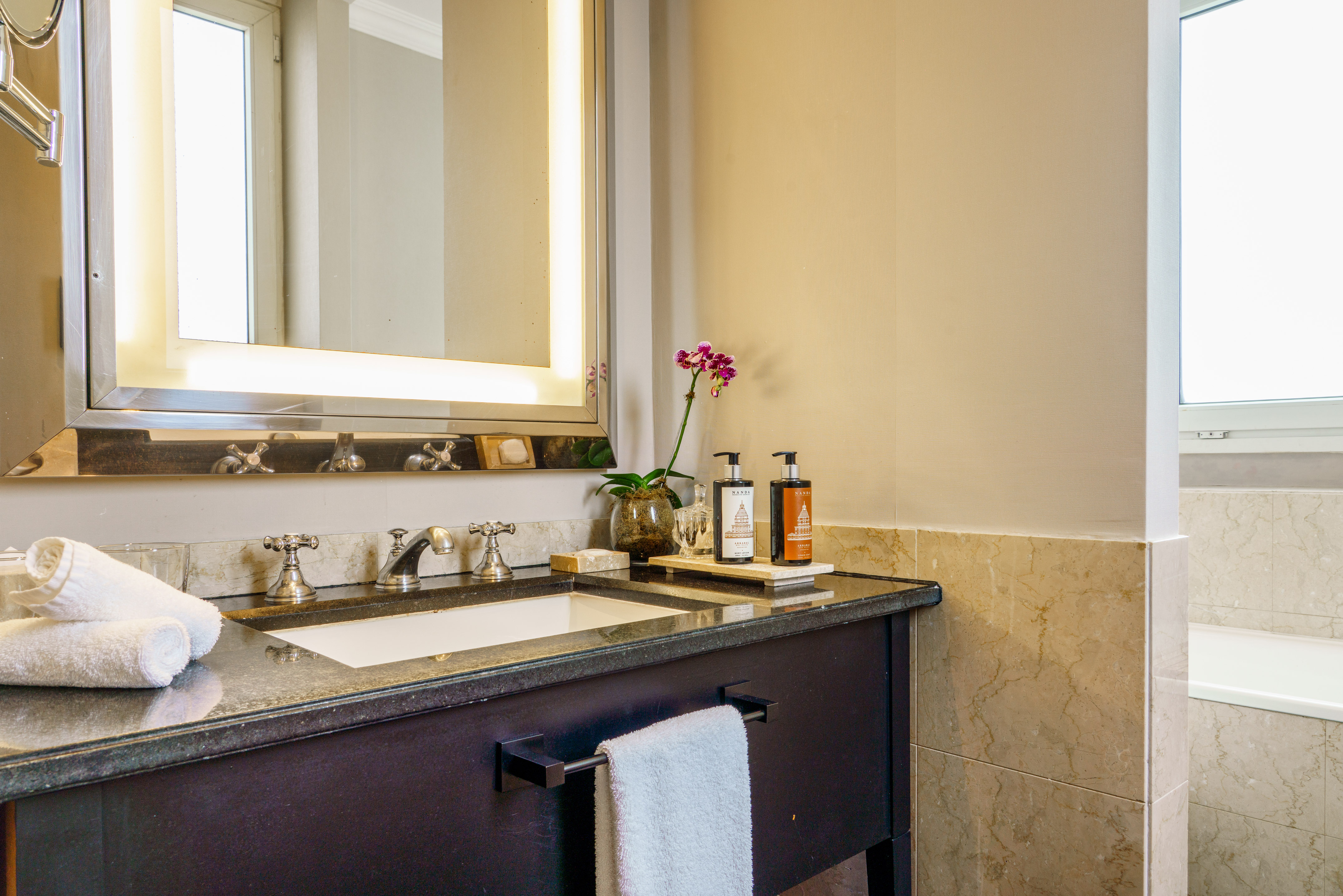 Hotel bathroom vanity, granite countertop, backlit mirror, sink, orchid.