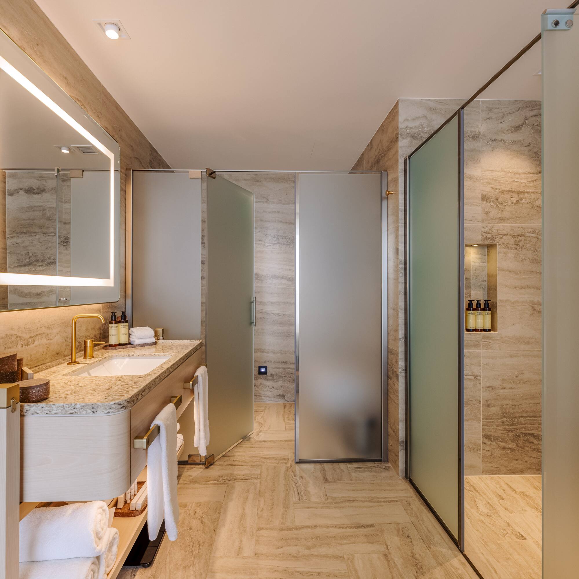 Luxurious modern bathroom with illuminated mirror, vanity, and frosted glass shower.