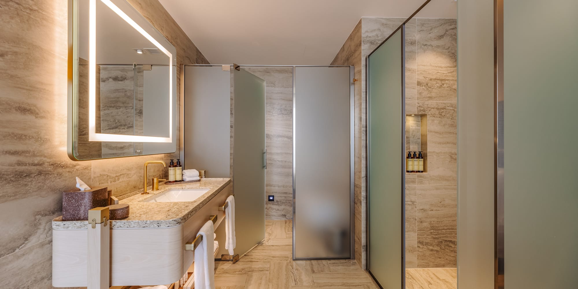 Luxurious modern bathroom with illuminated mirror, vanity, and frosted glass shower.