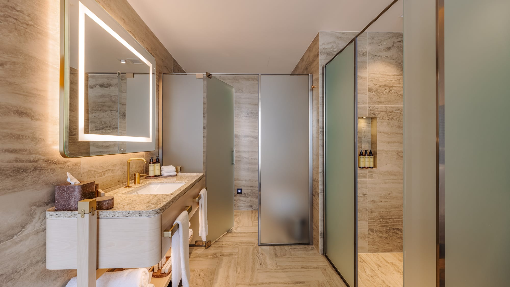 Luxurious modern bathroom with illuminated mirror, vanity, and frosted glass shower.