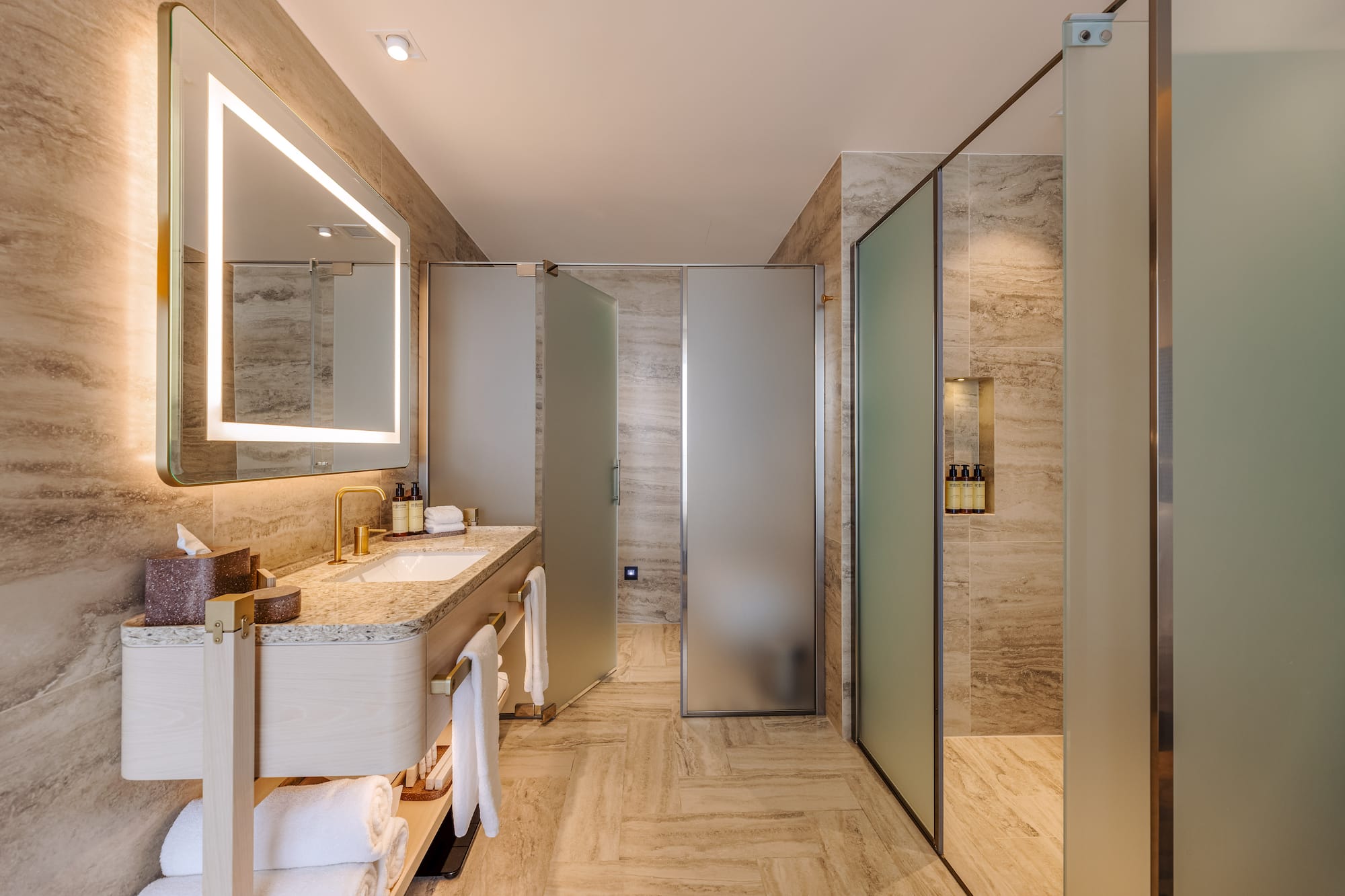 Luxurious modern bathroom with illuminated mirror, vanity, and frosted glass shower.