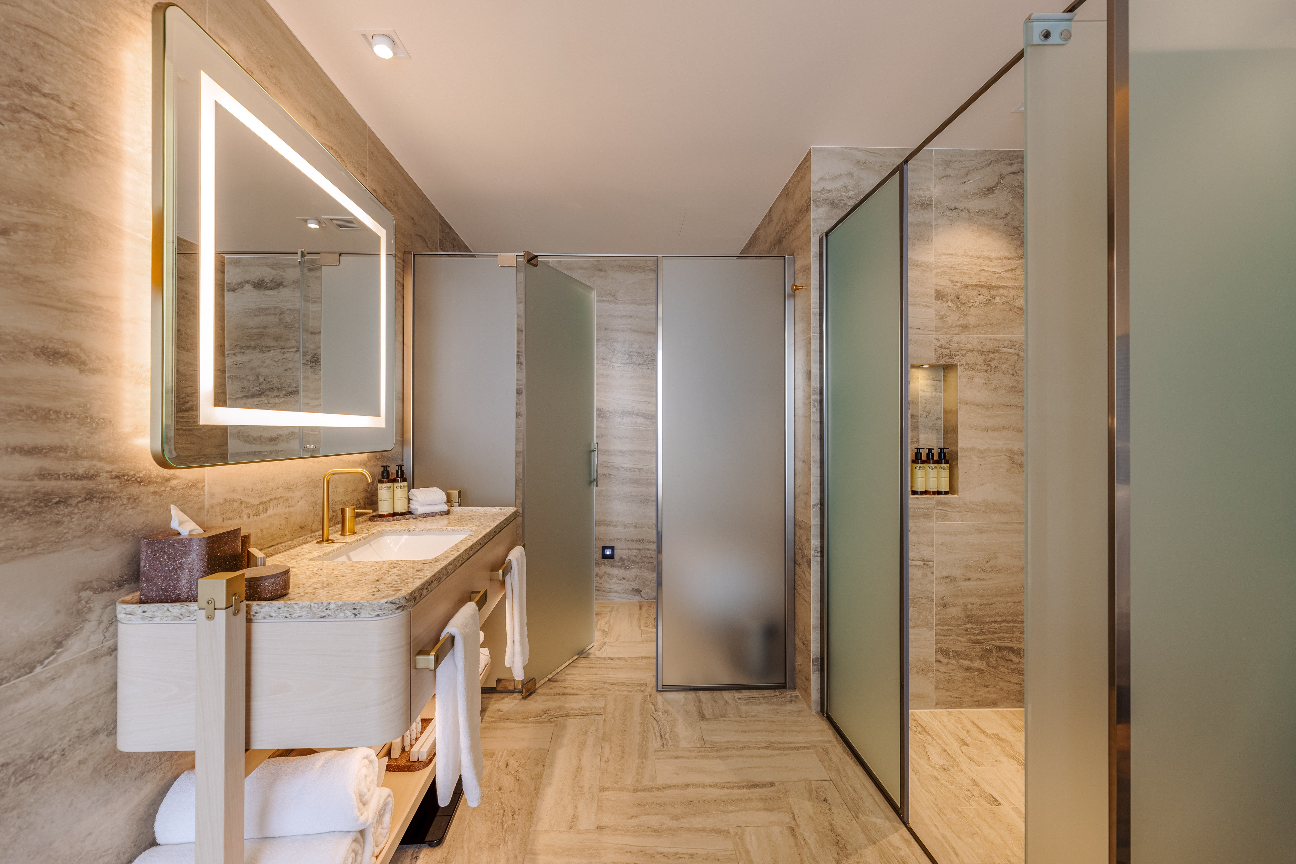 Luxurious modern bathroom with illuminated mirror, vanity, and frosted glass shower.