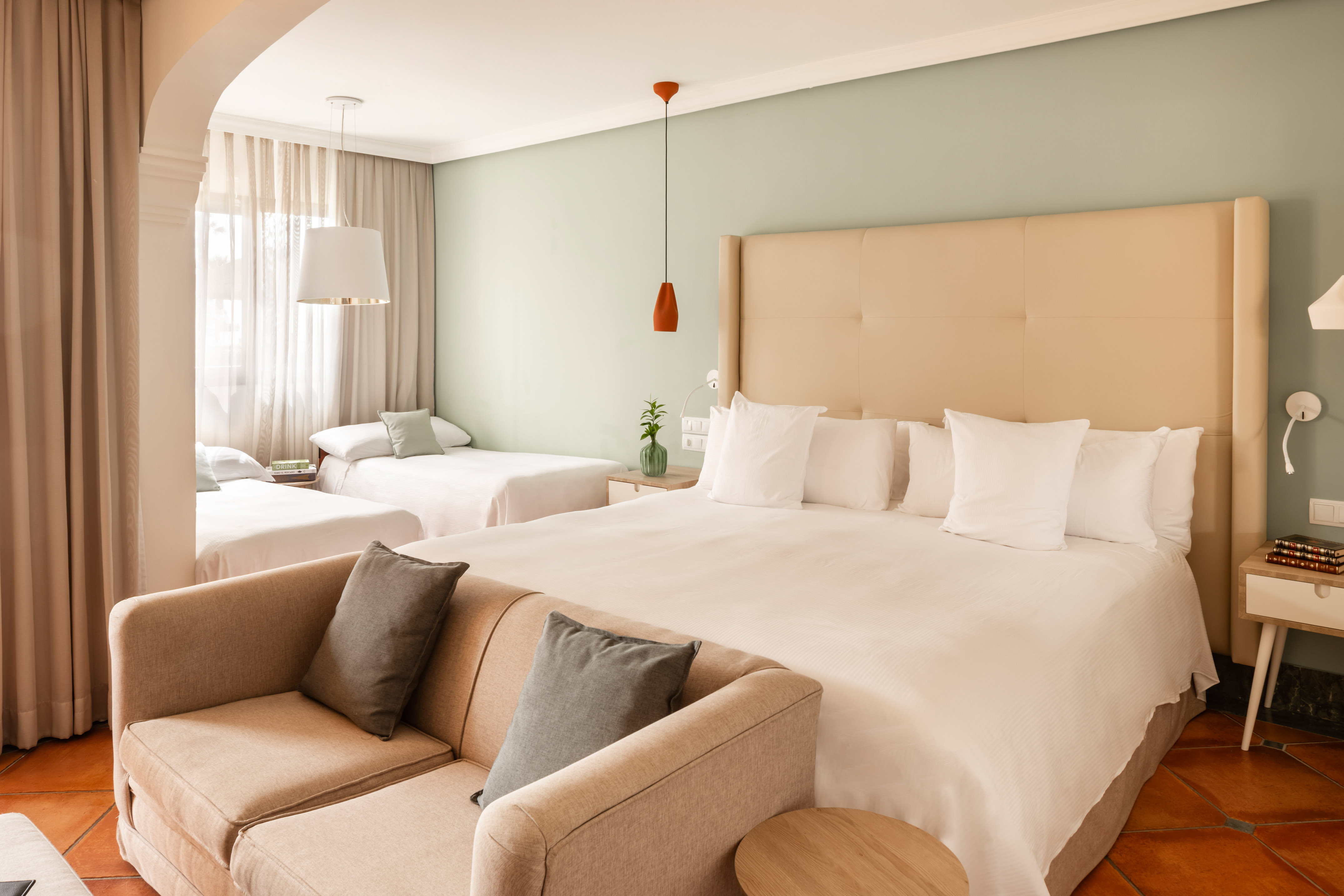 Hotel room with large bed, two single beds, and sofa, light green walls.