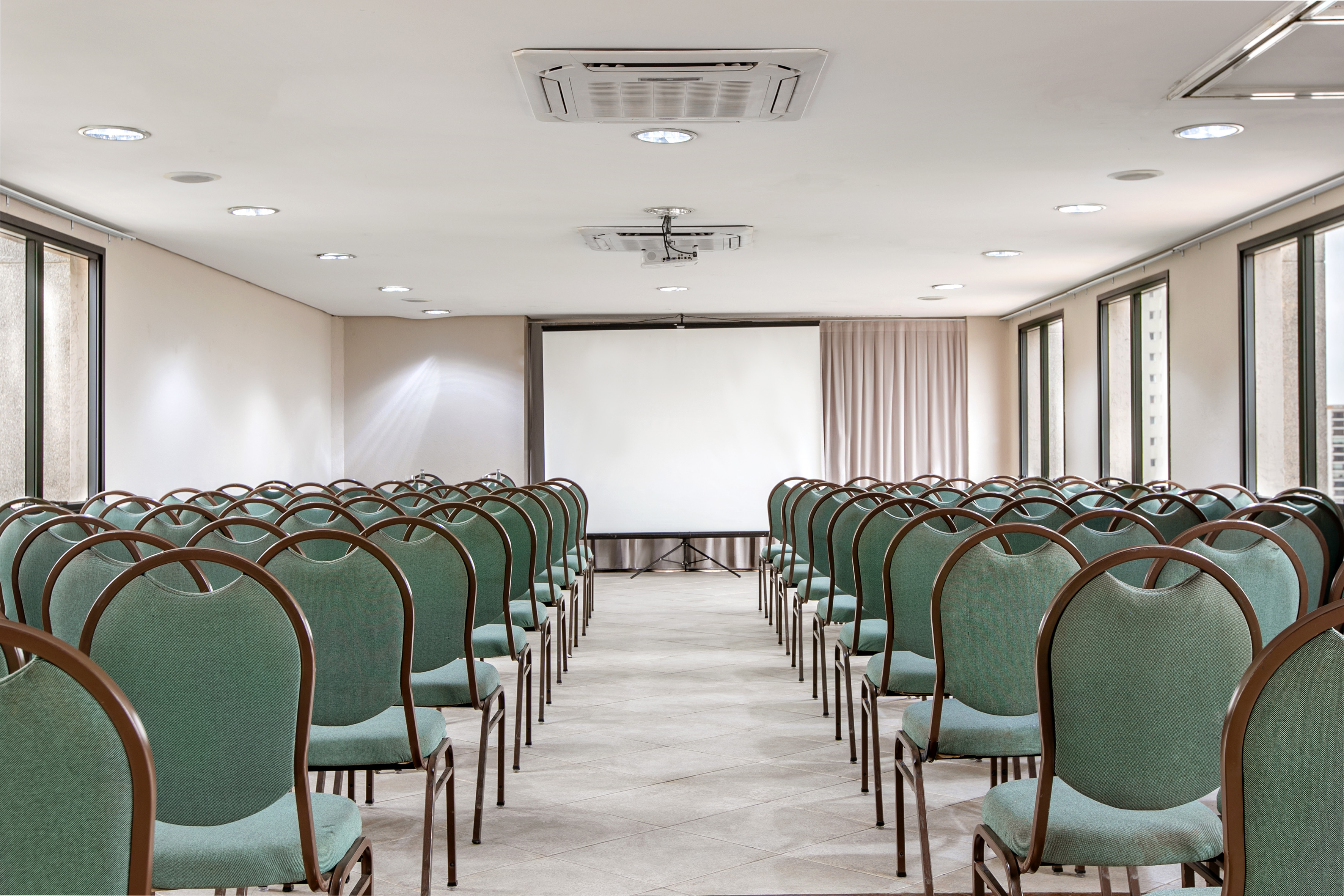 Conference room with green chairs, projector screen, and ceiling projector.