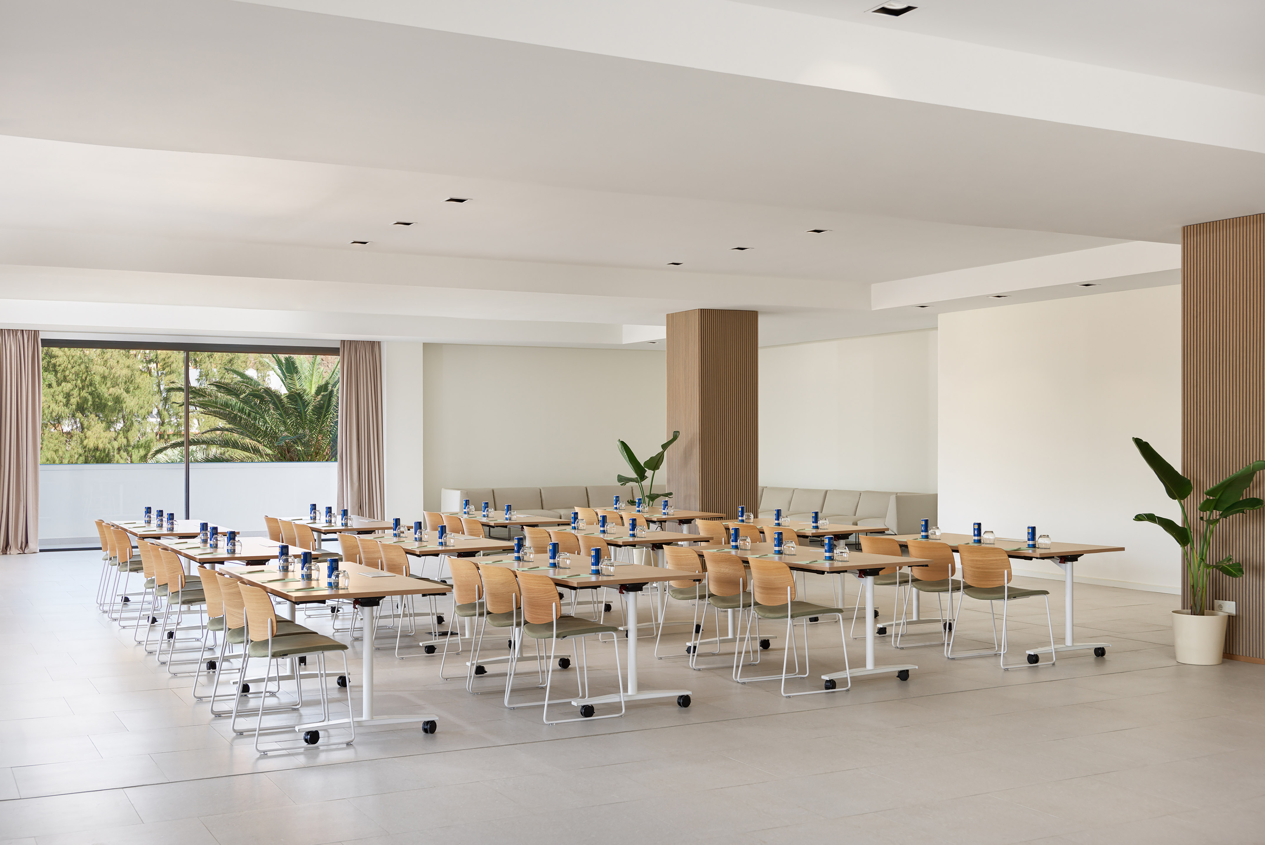 Modern meeting room with flexible tables, chairs, natural light, and potted plants.